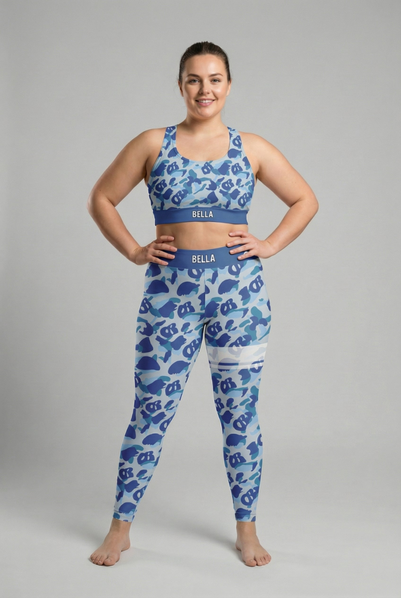 Front view of blue camouflage sports bra featuring hidden 'OB' monogram shapes in sky blue and dark blue, with 'BELLA' printed on the slate blue waistband.