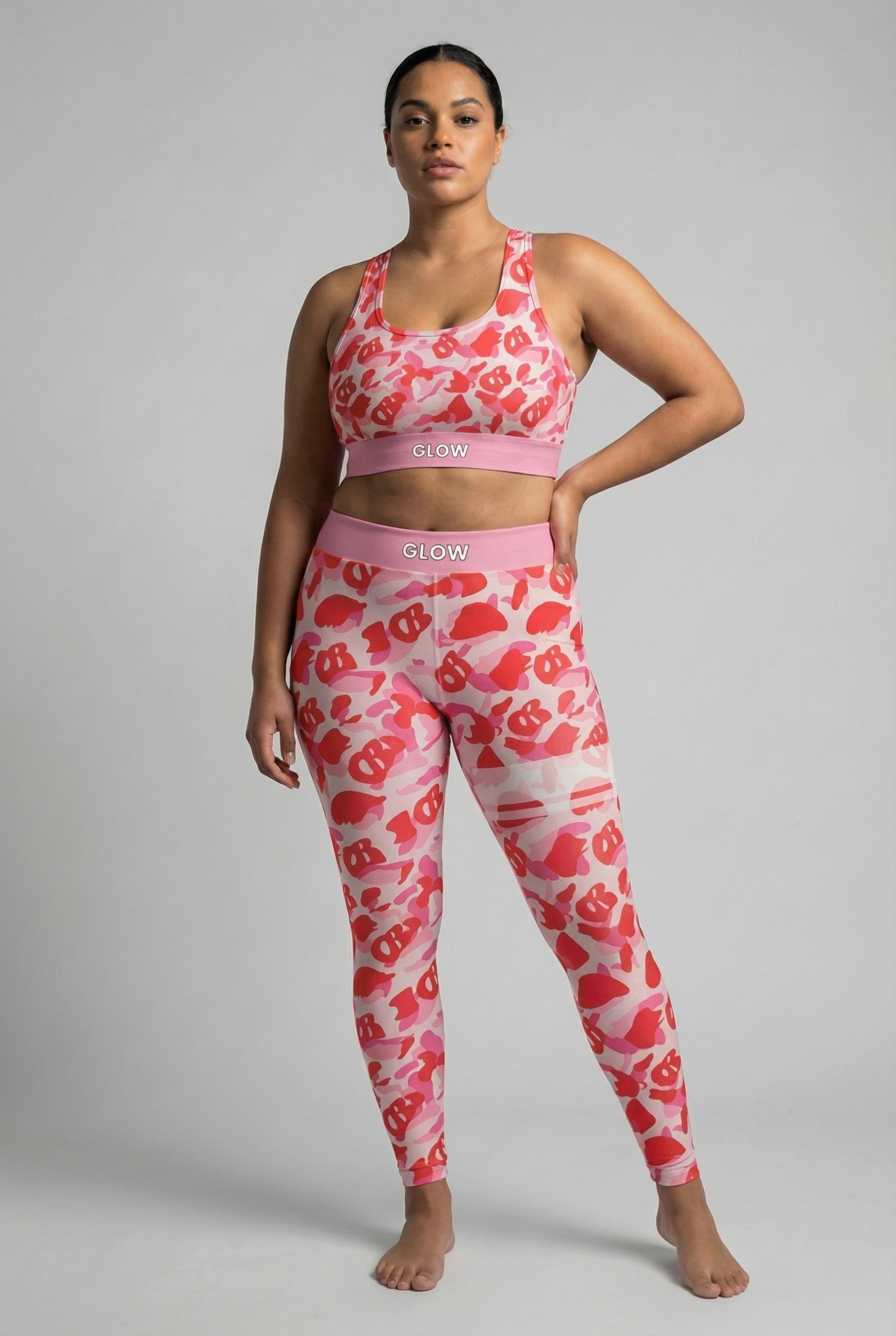 Close-up front view of pink camouflage sports bra featuring hidden 'OB' monogram shapes in red, with 'GLOW' printed on the pastel pink waistband.