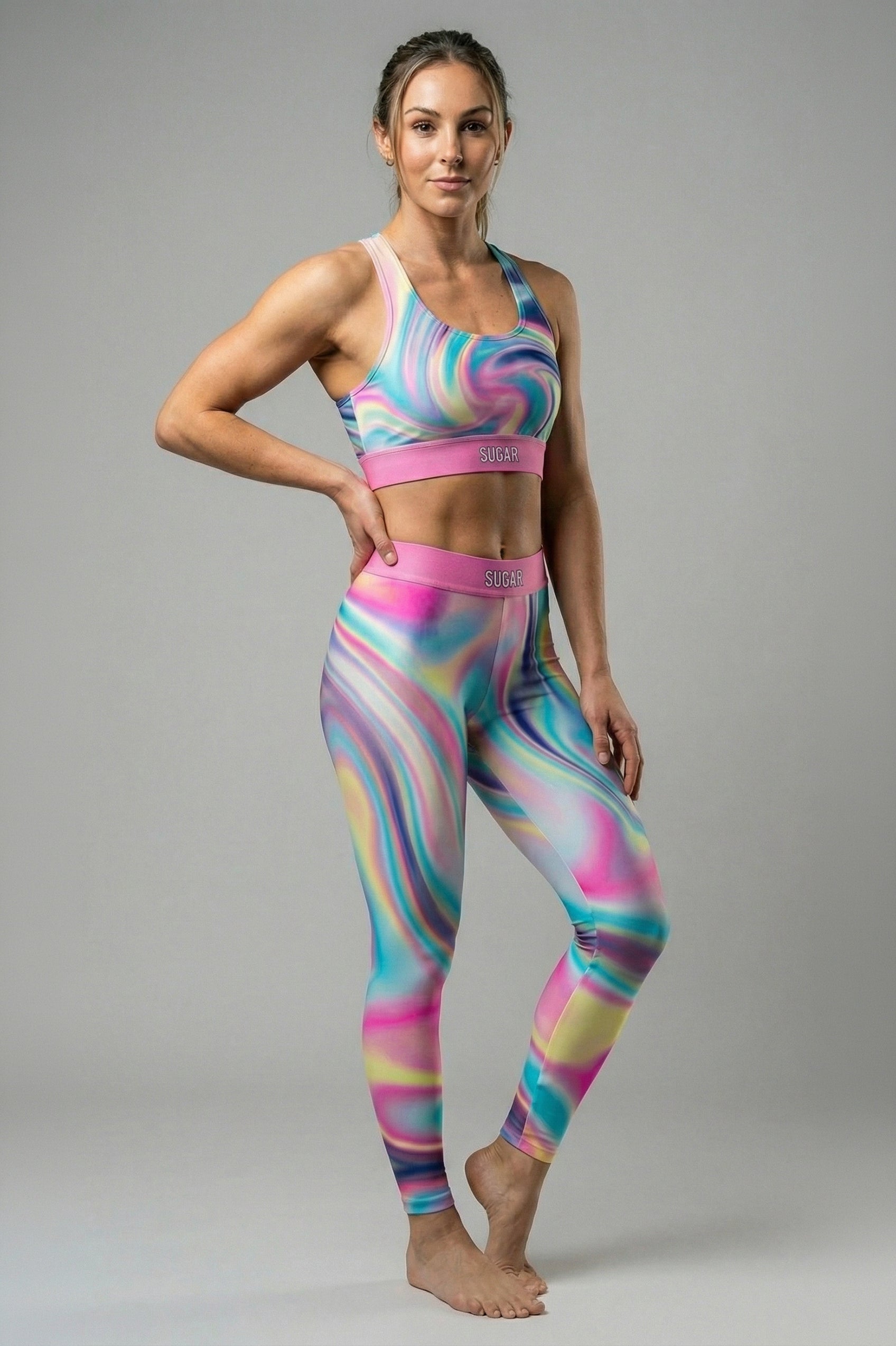 Front view of pastel tie-dye sports bra in baby blue, pink, and pale yellow, featuring 'SUGAR' printed on the pink waistband.
