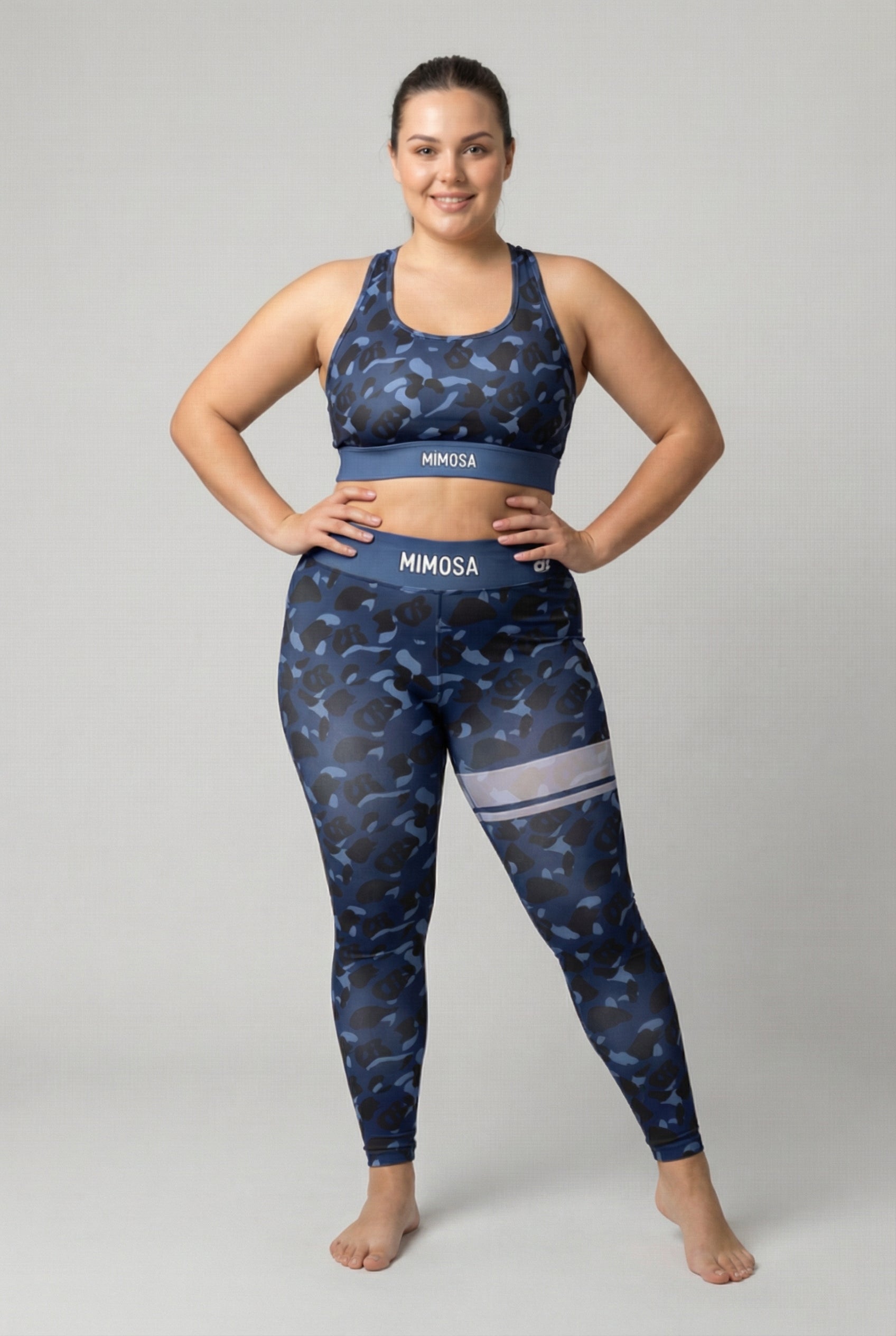 Front view of navy blue camouflage sports bra featuring hidden 'OB' monogram shapes in dark blue and black, with 'MIMOSA' printed on the navy waistband.