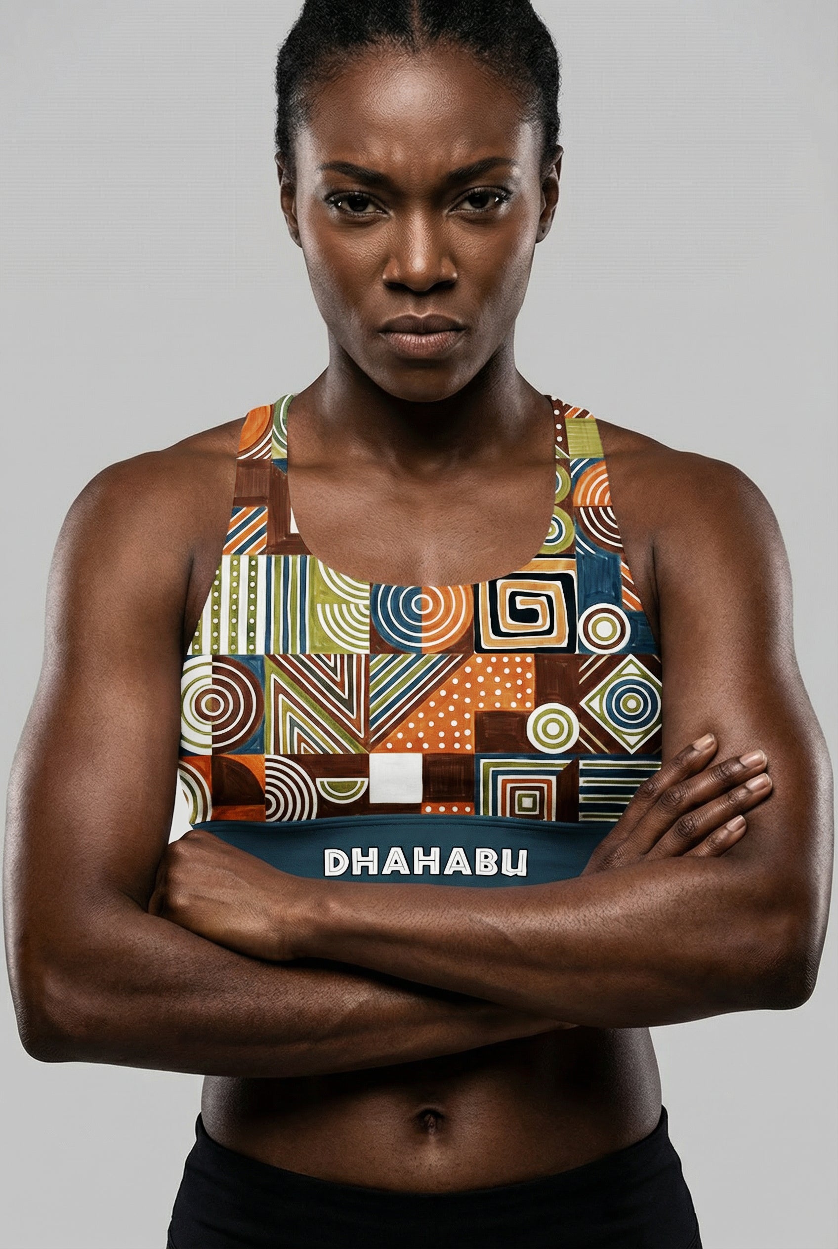 Front view of a dark-skinned model with arms crossed, wearing a tribal geometric pattern sports bra with 'DHAHABU' printed on the teal waistband.