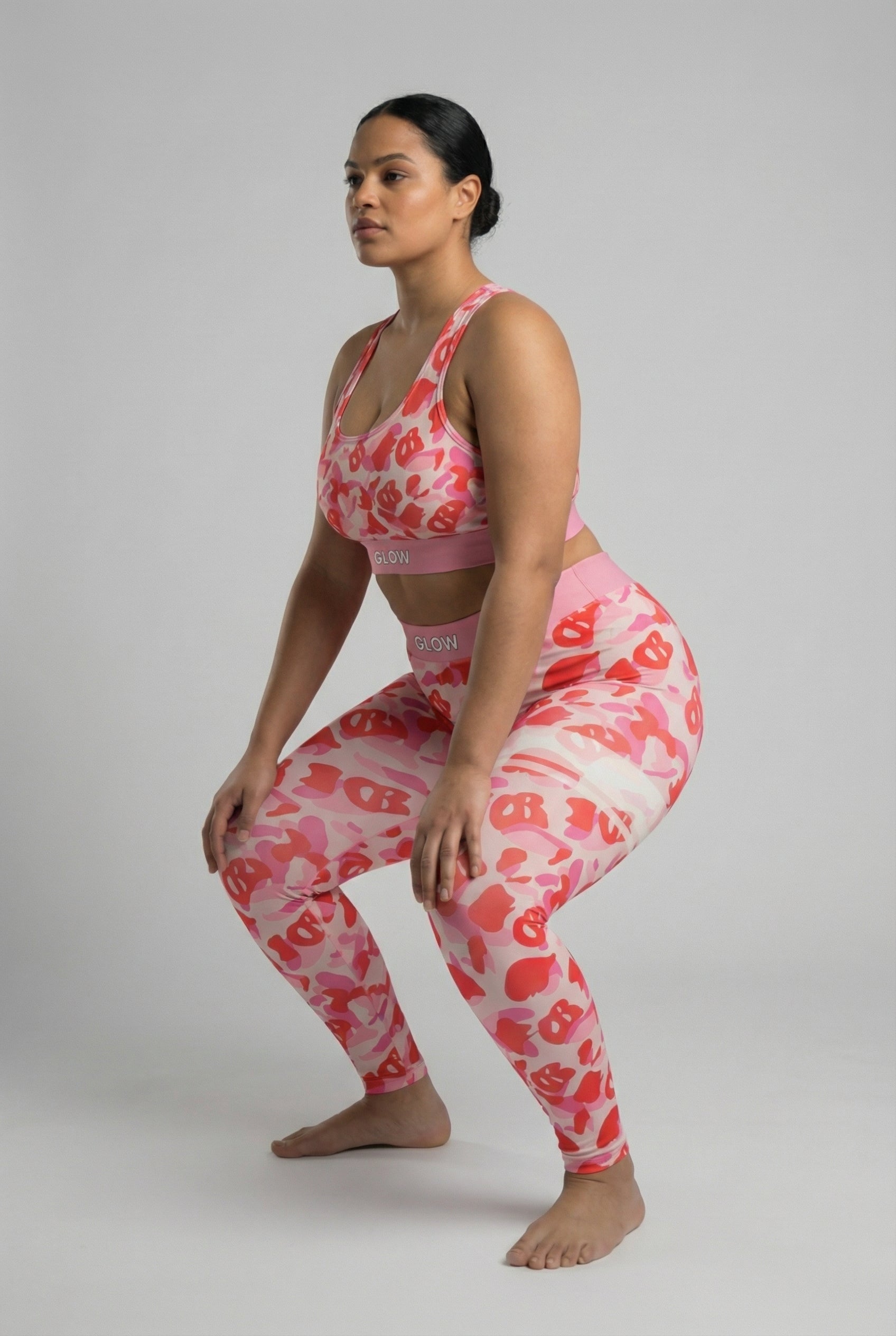 Close-up front view of pink camouflage sports bra featuring hidden 'OB' monogram shapes in red, with 'GLOW' printed on the pastel pink waistband.
