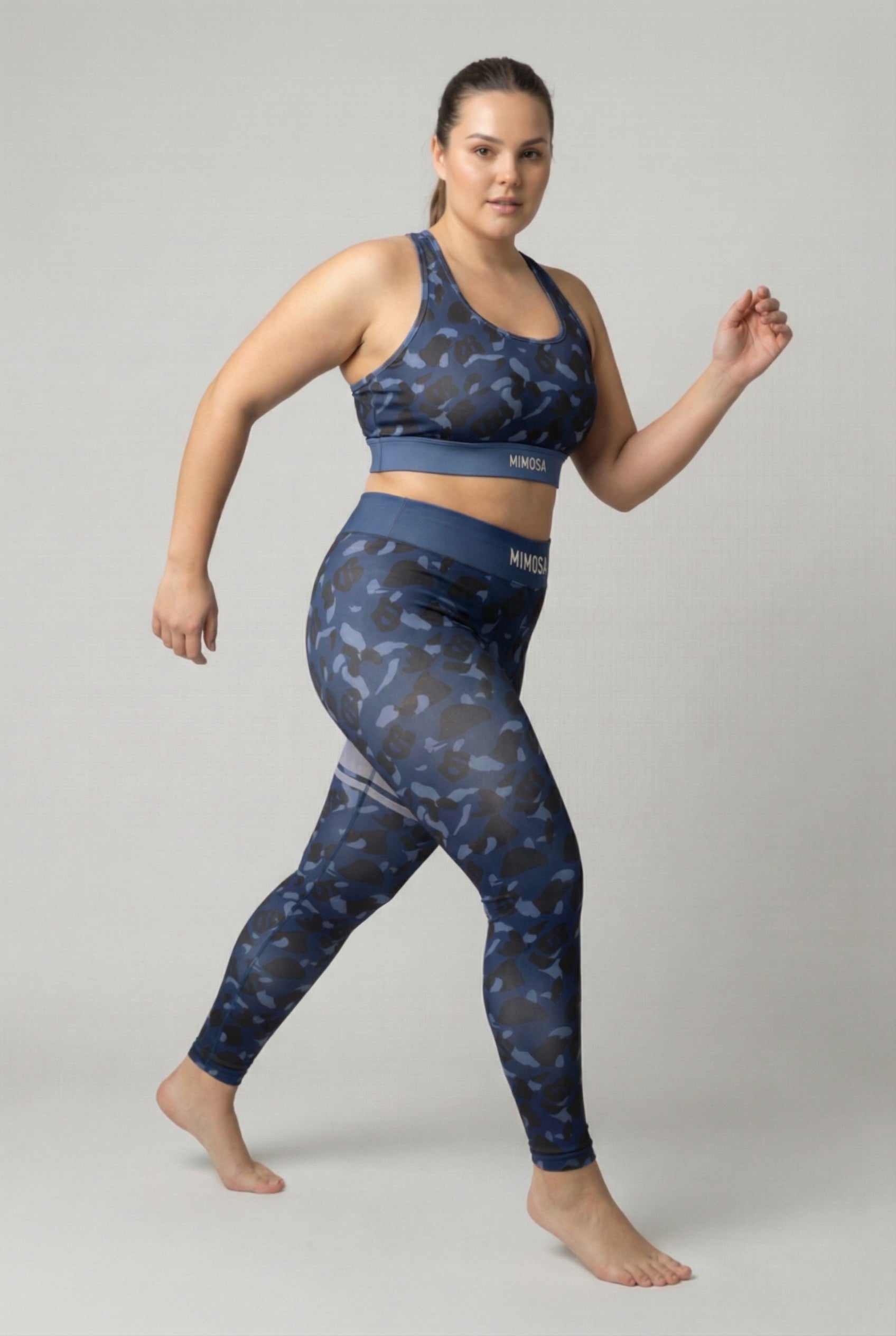 Front view of navy blue camouflage sports bra featuring hidden 'OB' monogram shapes in dark blue and black, with 'MIMOSA' printed on the navy waistband.