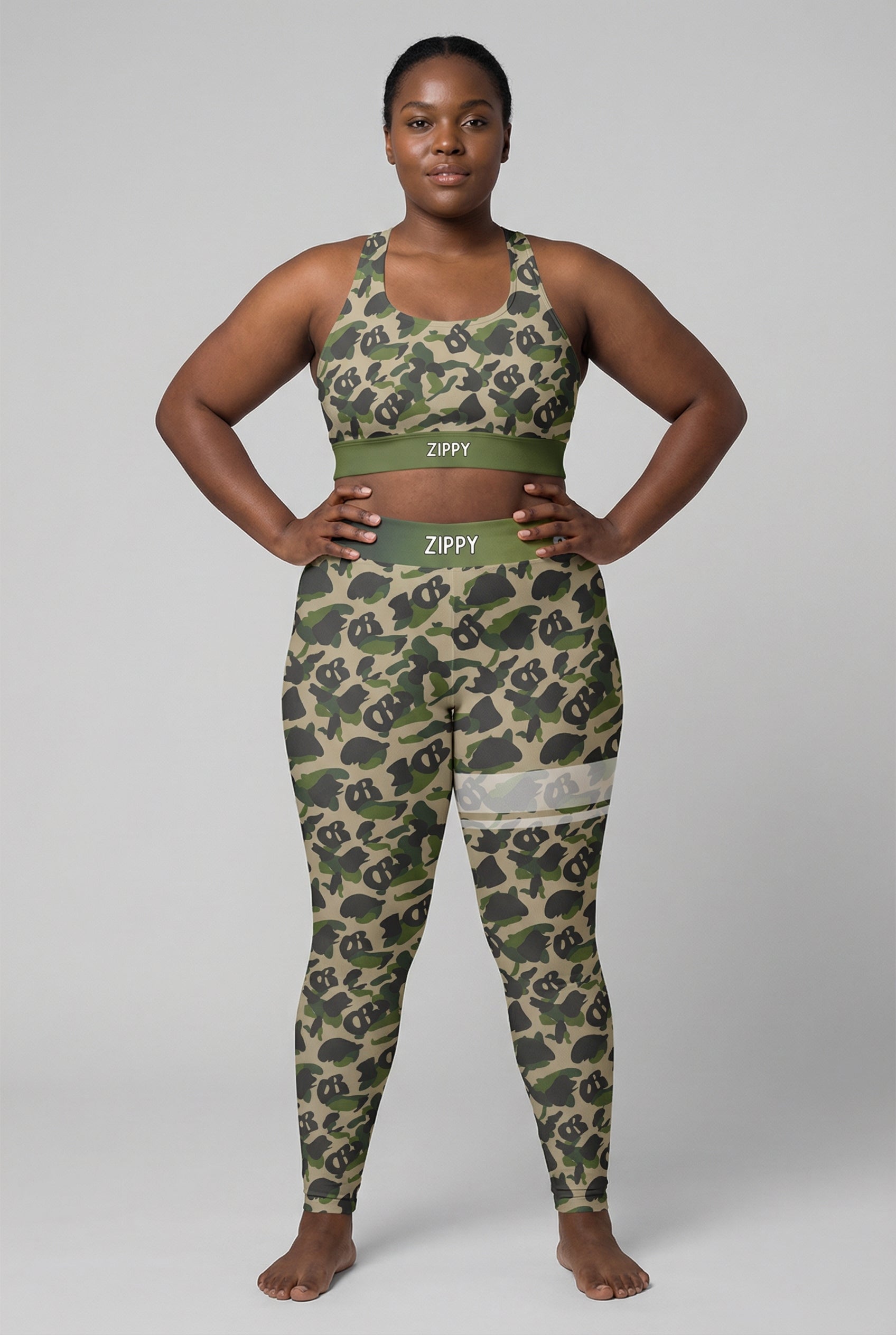 Front view of green camouflage sports bra featuring hidden 'OB' monogram shapes in olive and tan, with 'ZIPPY' printed on the olive green waistband.
