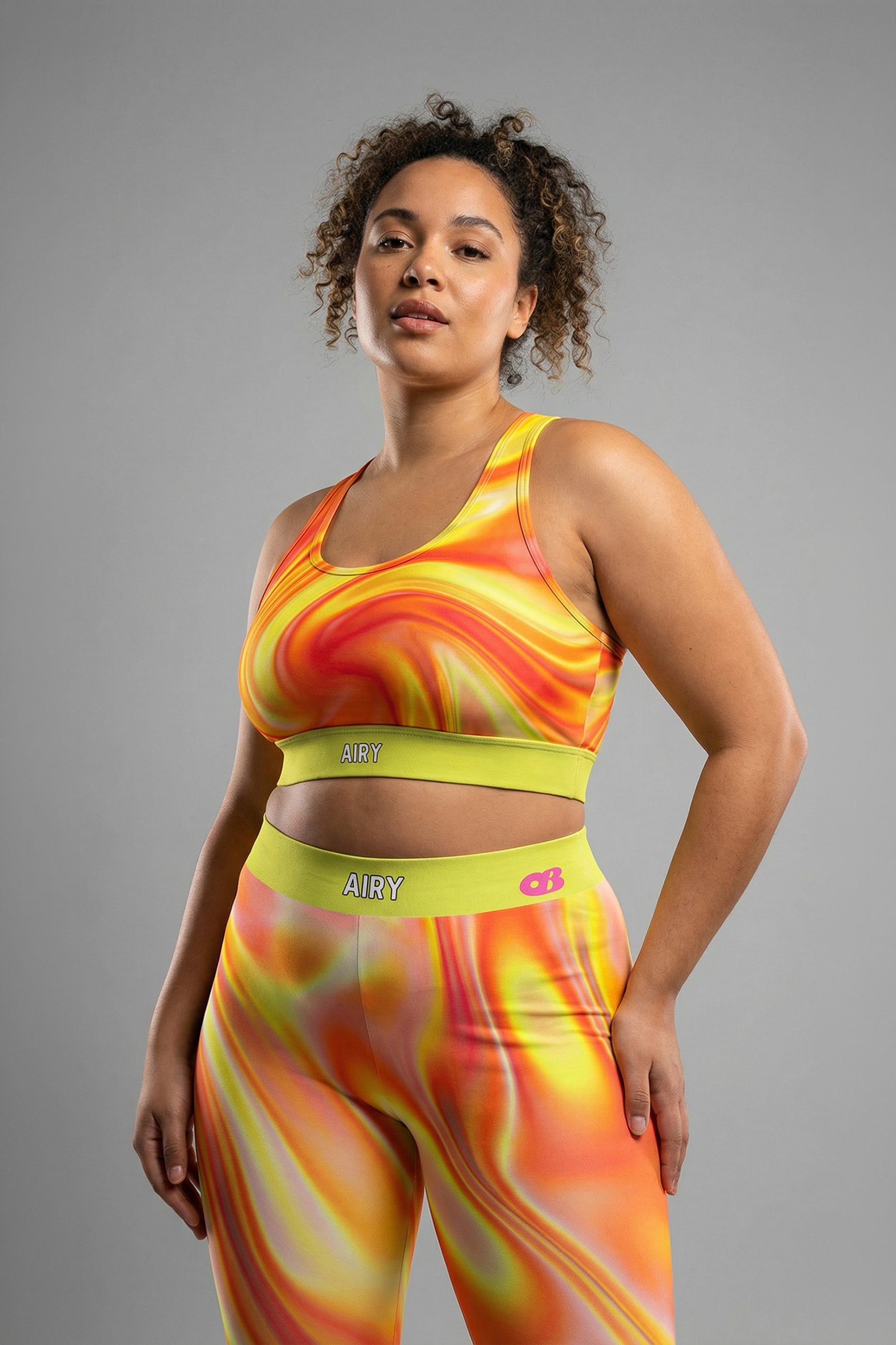 Front view of tie-dye sports bra in orange, yellow, and red swirls, featuring 'AIRY' printed on the neon lime green waistband.