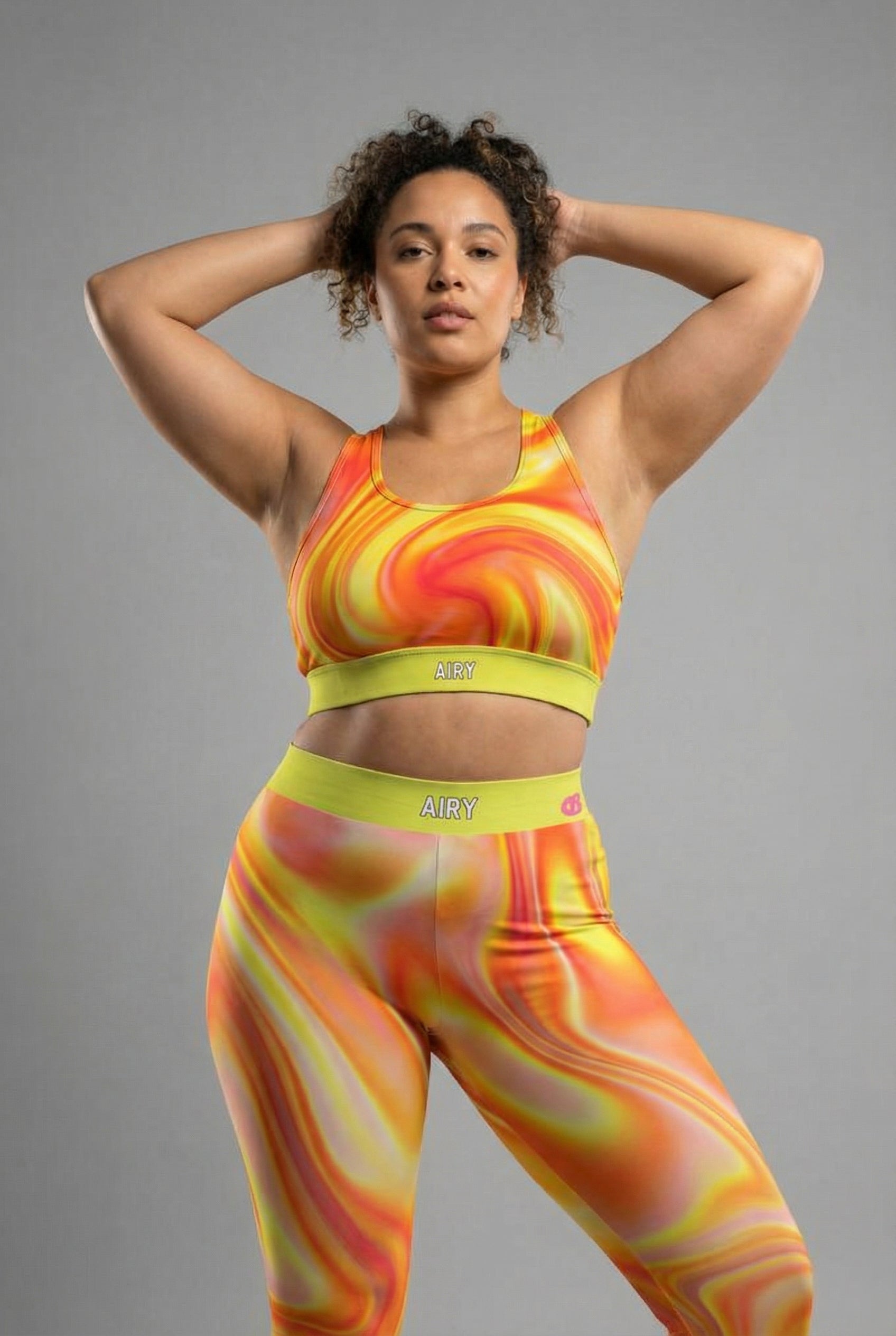 Front view of tie-dye sports bra in orange, yellow, and red swirls, featuring 'AIRY' printed on the neon lime green waistband.