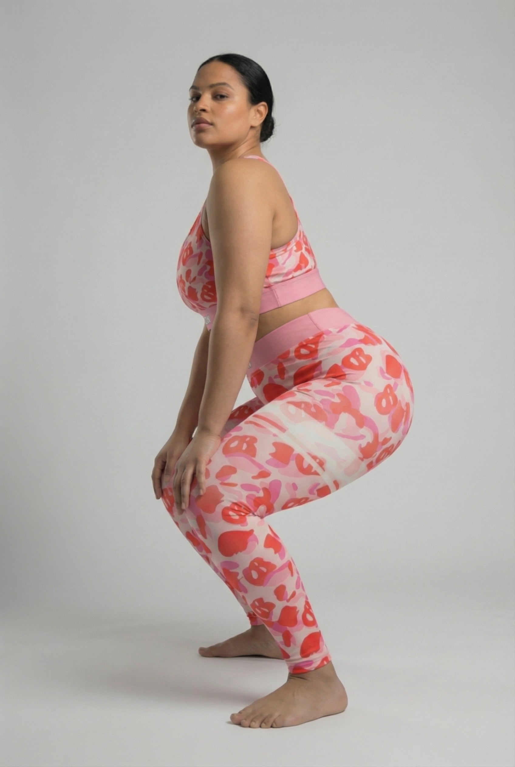 Close-up front view of pink camouflage sports bra featuring hidden 'OB' monogram shapes in red, with 'GLOW' printed on the pastel pink waistband.