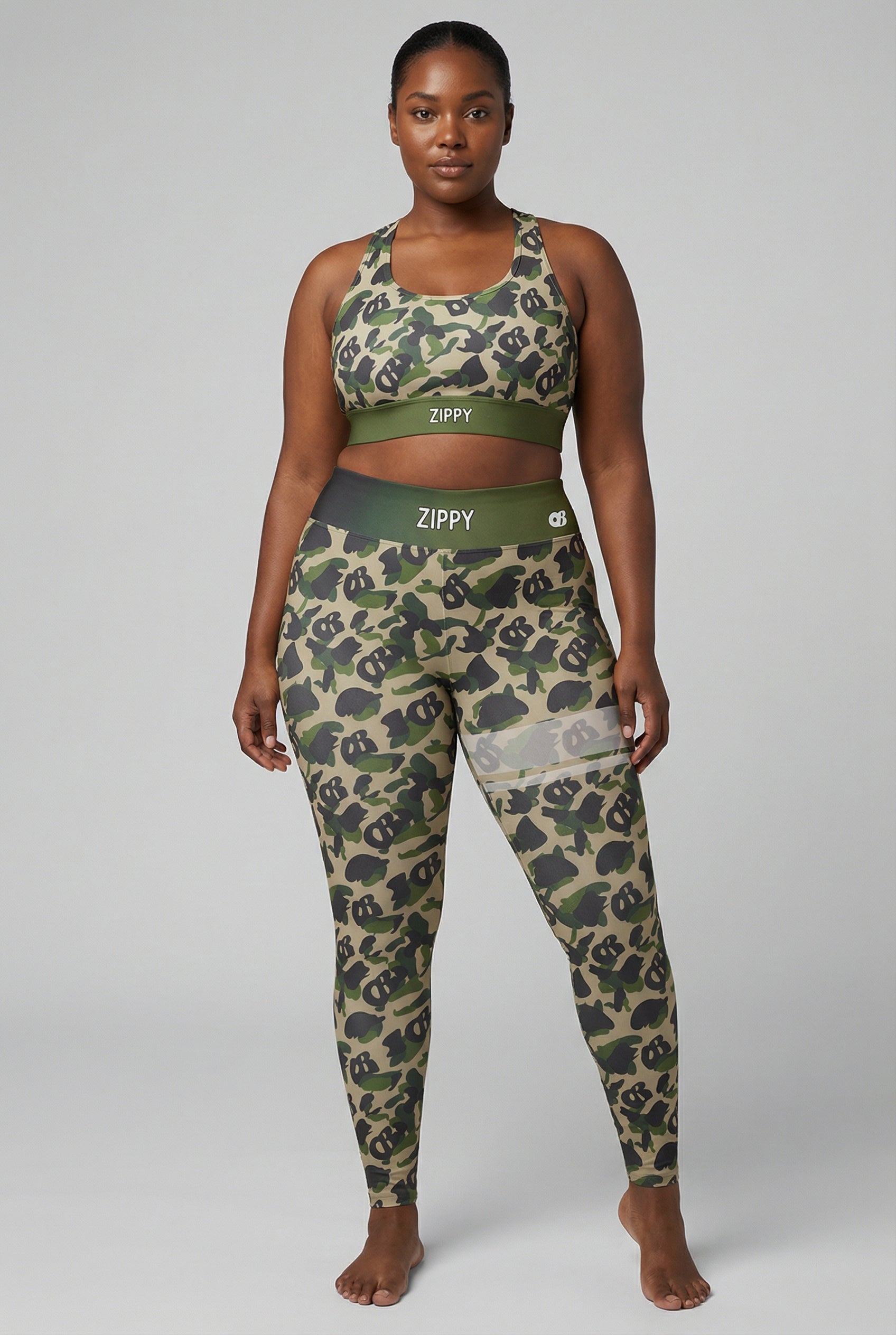 Front view of green camouflage sports bra featuring hidden 'OB' monogram shapes in olive and tan, with 'ZIPPY' printed on the olive green waistband.