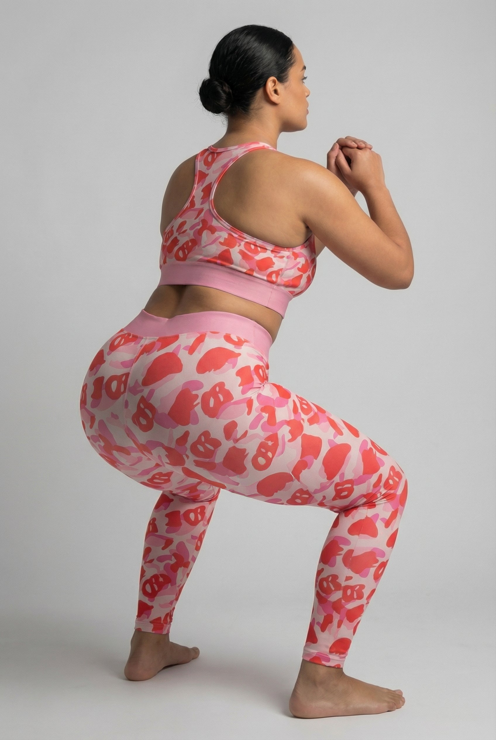 Front view of pink camouflage leggings with hidden 'OB' monogram shapes, featuring white stripes on the left thigh and 'GLOW' printed on the pastel pink waistband.