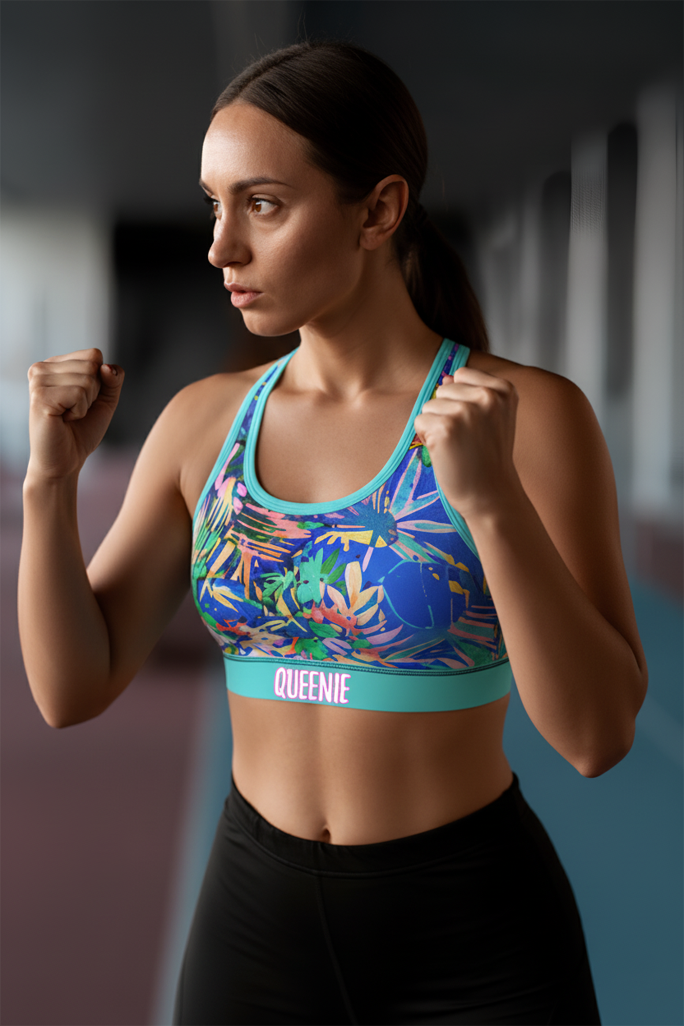 Woman wearing a colorful sports bra with 'QUEENIE' branding in an indoor setting.