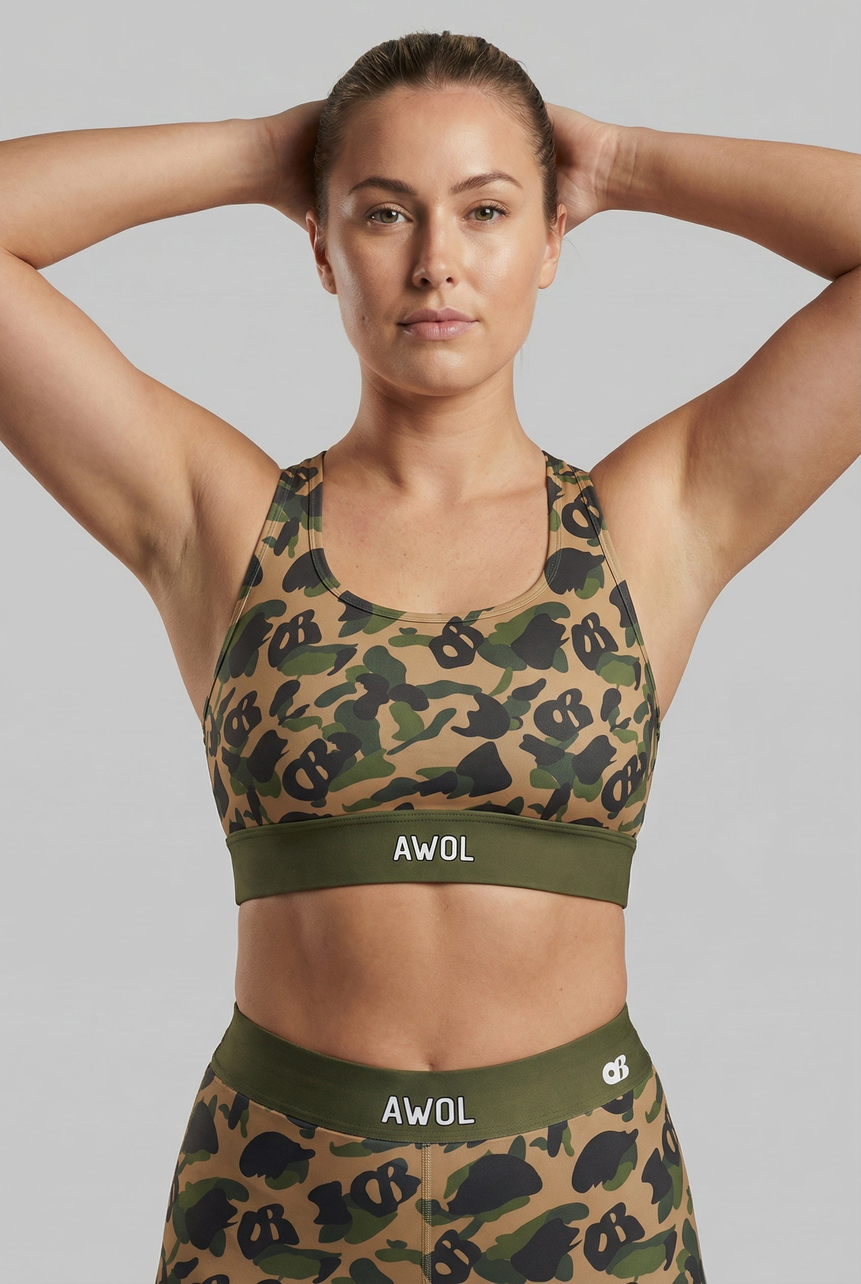 Front view of green camouflage sports bra featuring hidden 'OB' monogram shapes in olive, tan, and black, with 'AWOL' printed on the olive green waistband.