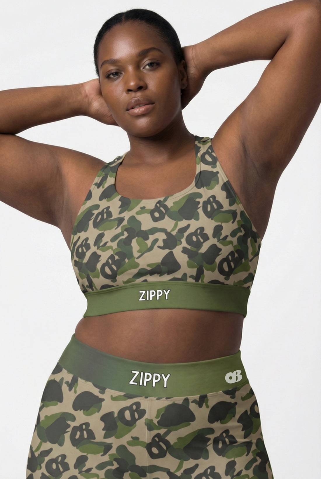 Front view of green camouflage sports bra featuring hidden 'OB' monogram shapes in olive and tan, with 'ZIPPY' printed on the olive green waistband.