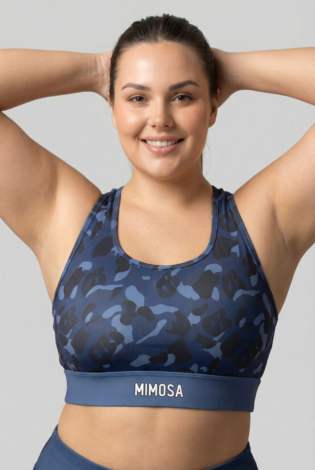 Front view of navy blue camouflage sports bra featuring hidden 'OB' monogram shapes in dark blue and black, with 'MIMOSA' printed on the navy waistband.