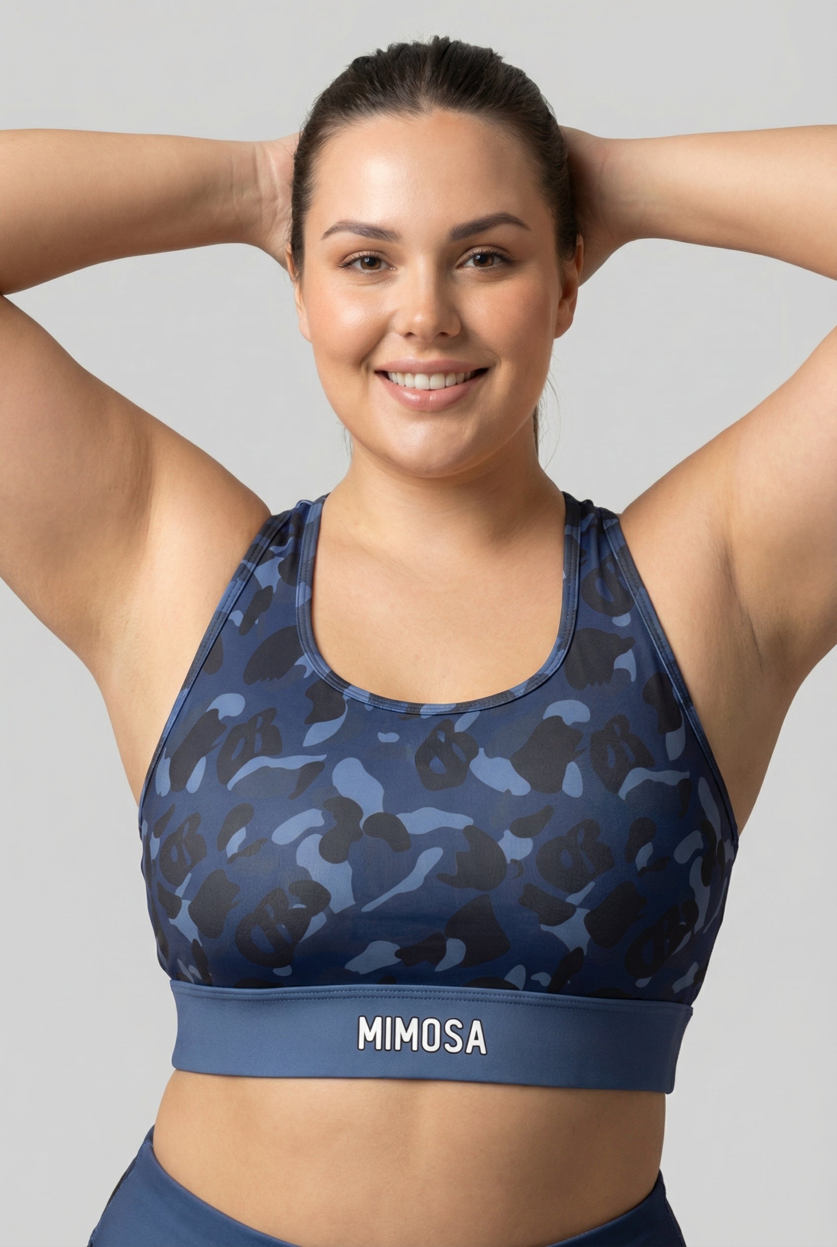 Front view of navy blue camouflage sports bra featuring hidden 'OB' monogram shapes in dark blue and black, with 'MIMOSA' printed on the navy waistband.