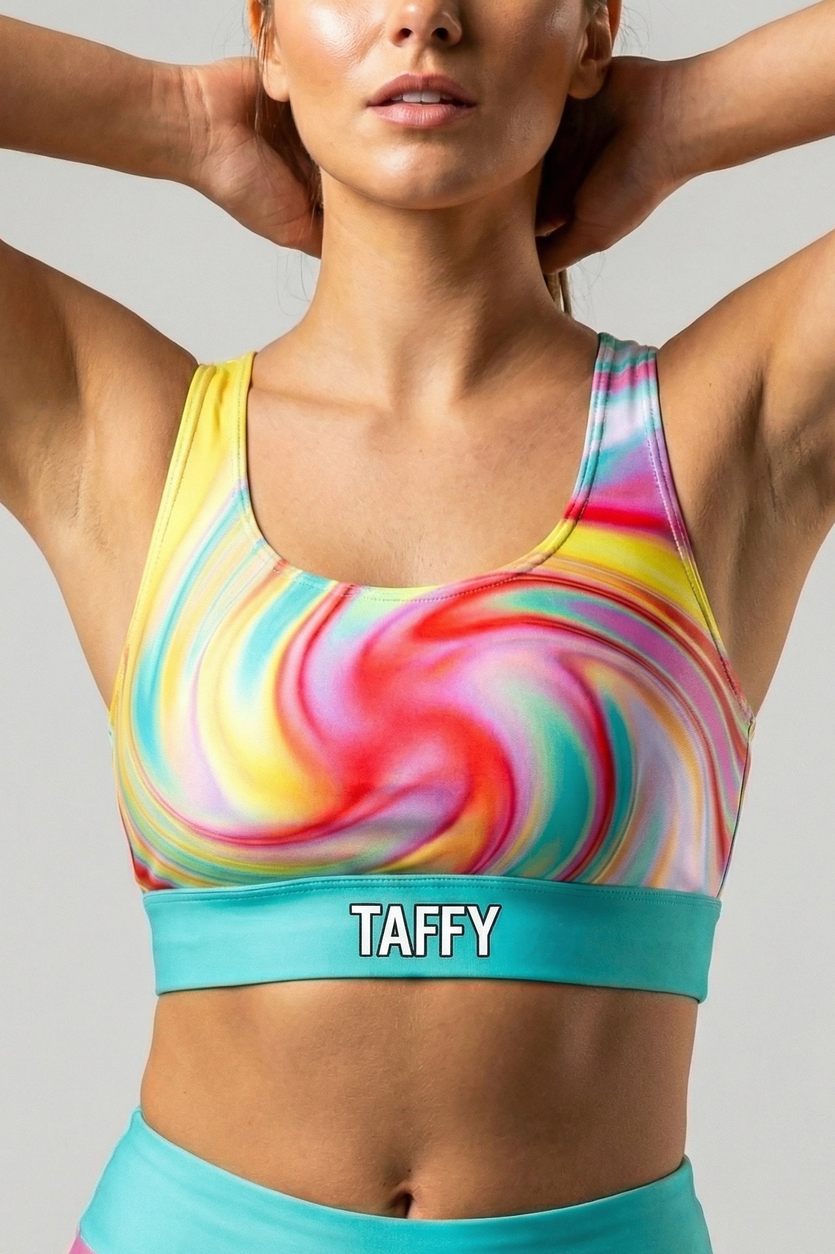 Front view of multi-color tie-dye sports bra with swirling yellow, pink, and red pattern, featuring 'TAFFY' printed on the bright turquoise waistband.