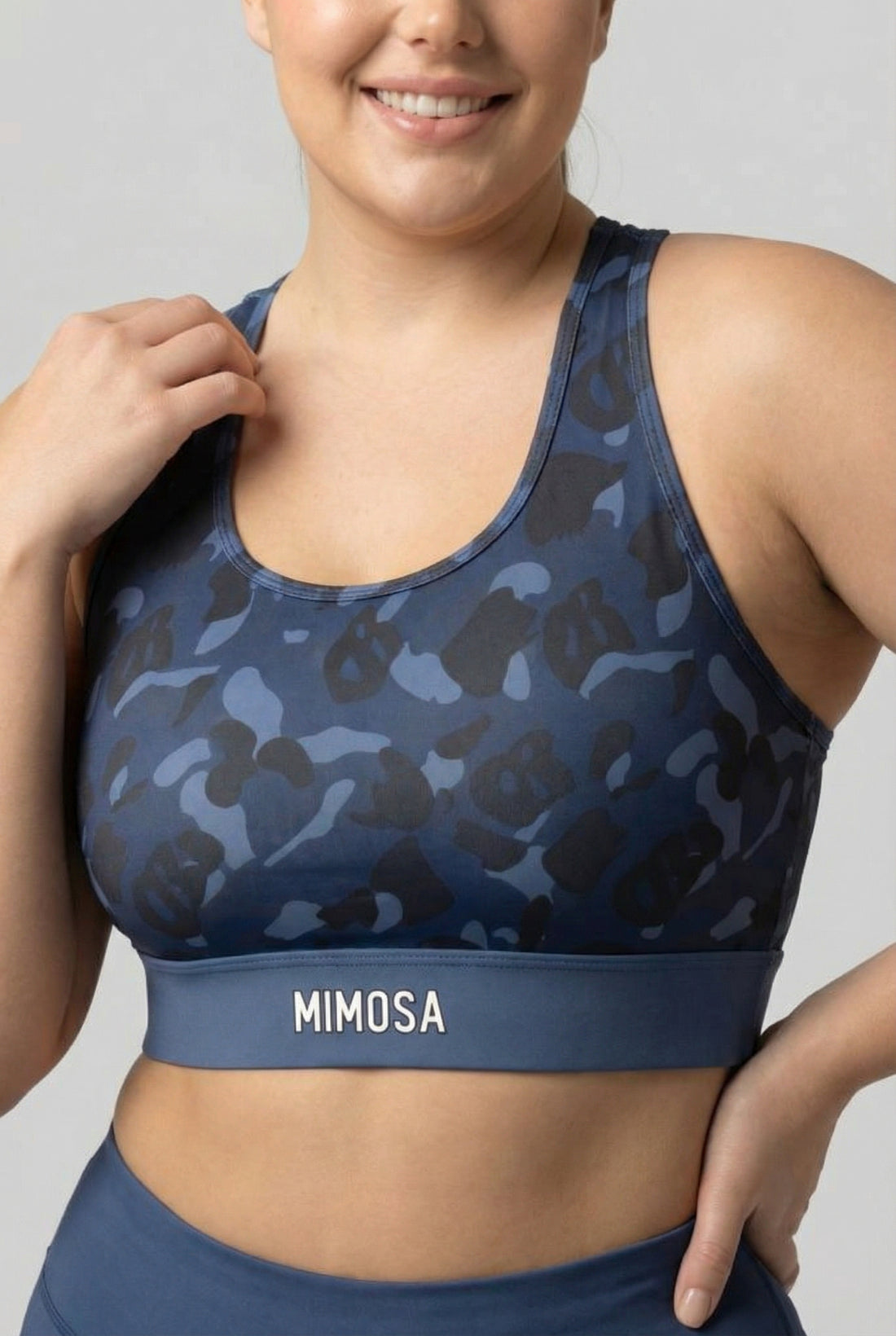 Front view of navy blue camouflage sports bra featuring hidden 'OB' monogram shapes in dark blue and black, with 'MIMOSA' printed on the navy waistband.