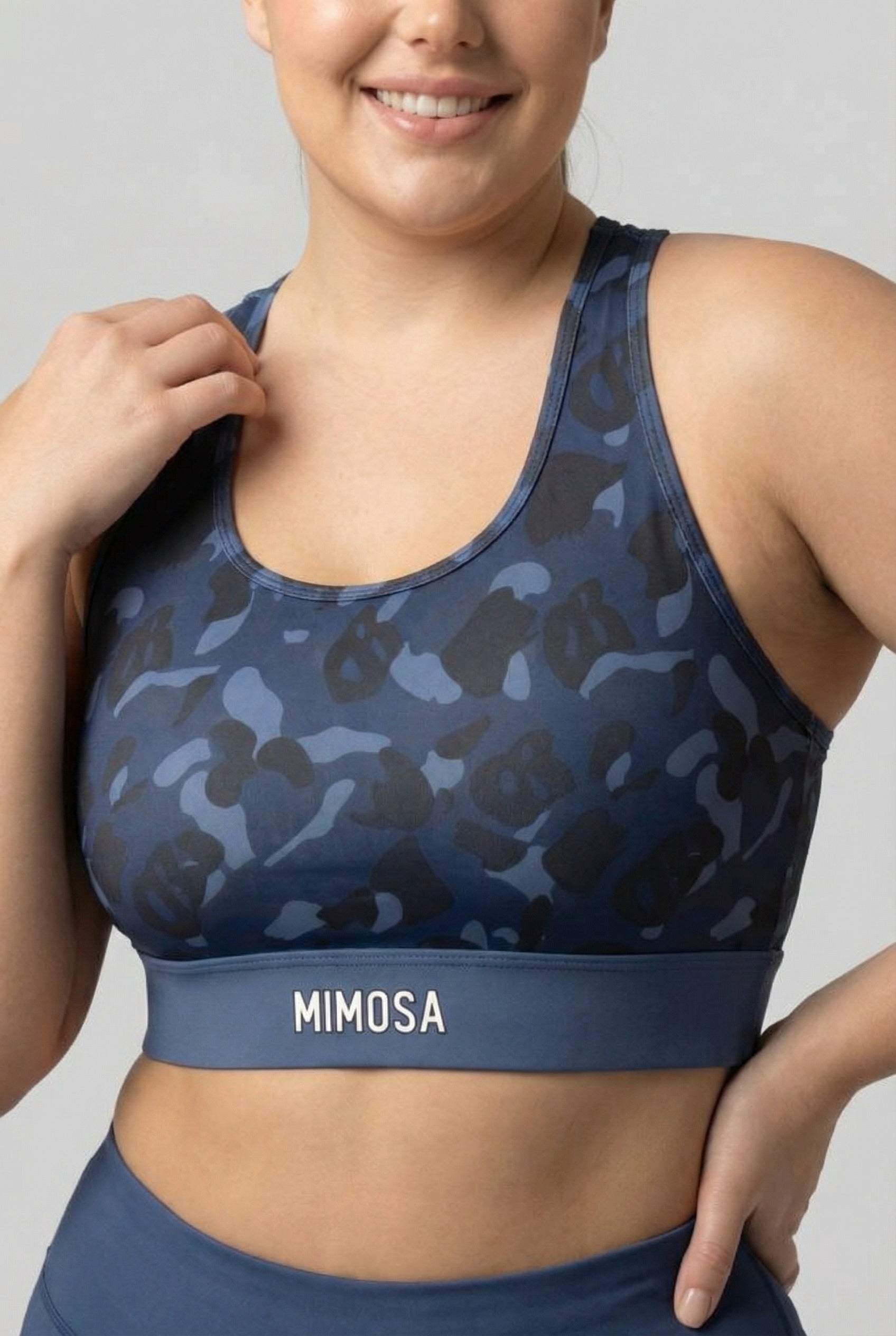 Front view of navy blue camouflage sports bra featuring hidden 'OB' monogram shapes in dark blue and black, with 'MIMOSA' printed on the navy waistband.