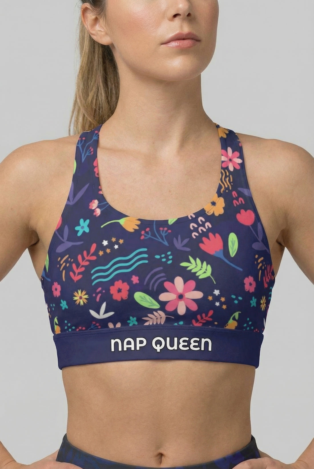 Woman wearing a colorful floral sports bra with 'Nap Queen' text on a gray background
