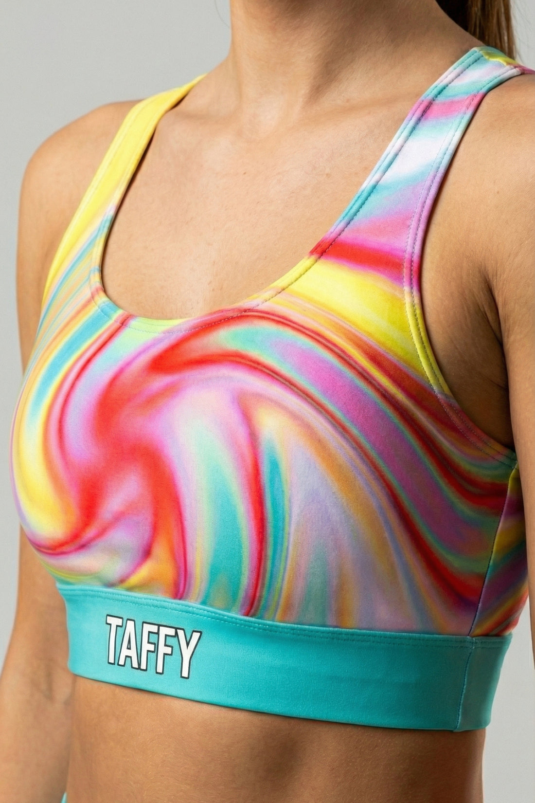 Front view of multi-color tie-dye sports bra with swirling yellow, pink, and red pattern, featuring 'TAFFY' printed on the bright turquoise waistband.