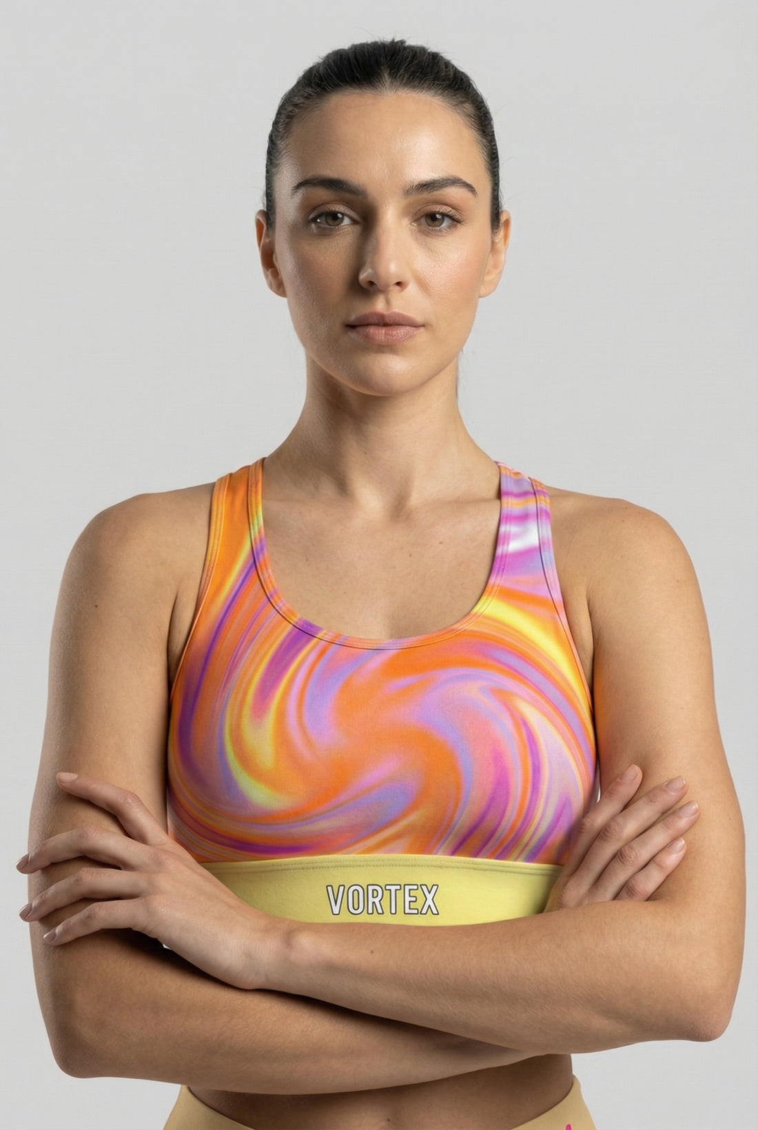 Front view of tie-dye sports bra with orange, purple, and yellow swirl pattern, featuring 'VORTEX' printed on the pastel yellow waistband.