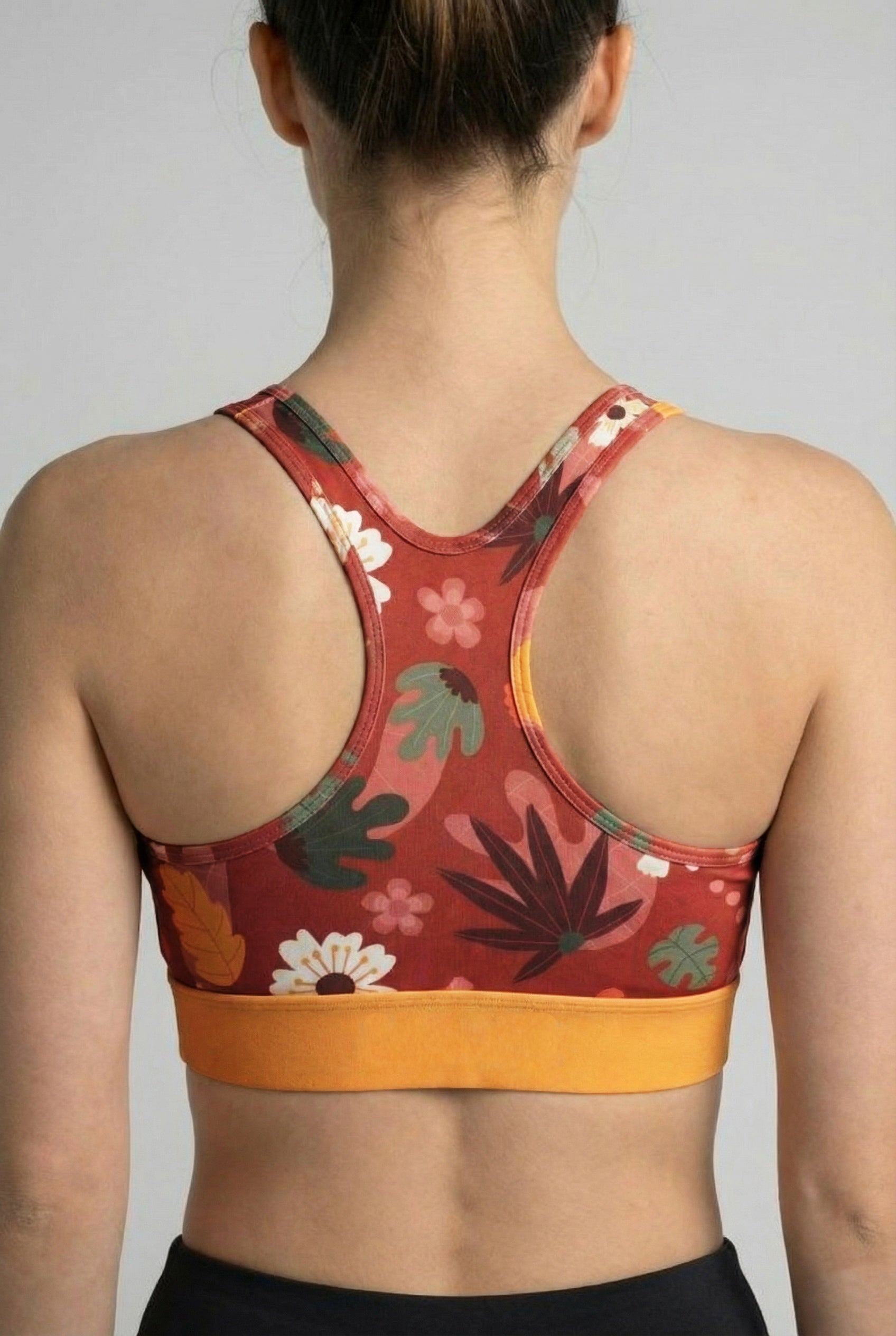 Floral-patterned sports bra with orange band worn by a person on a plain background