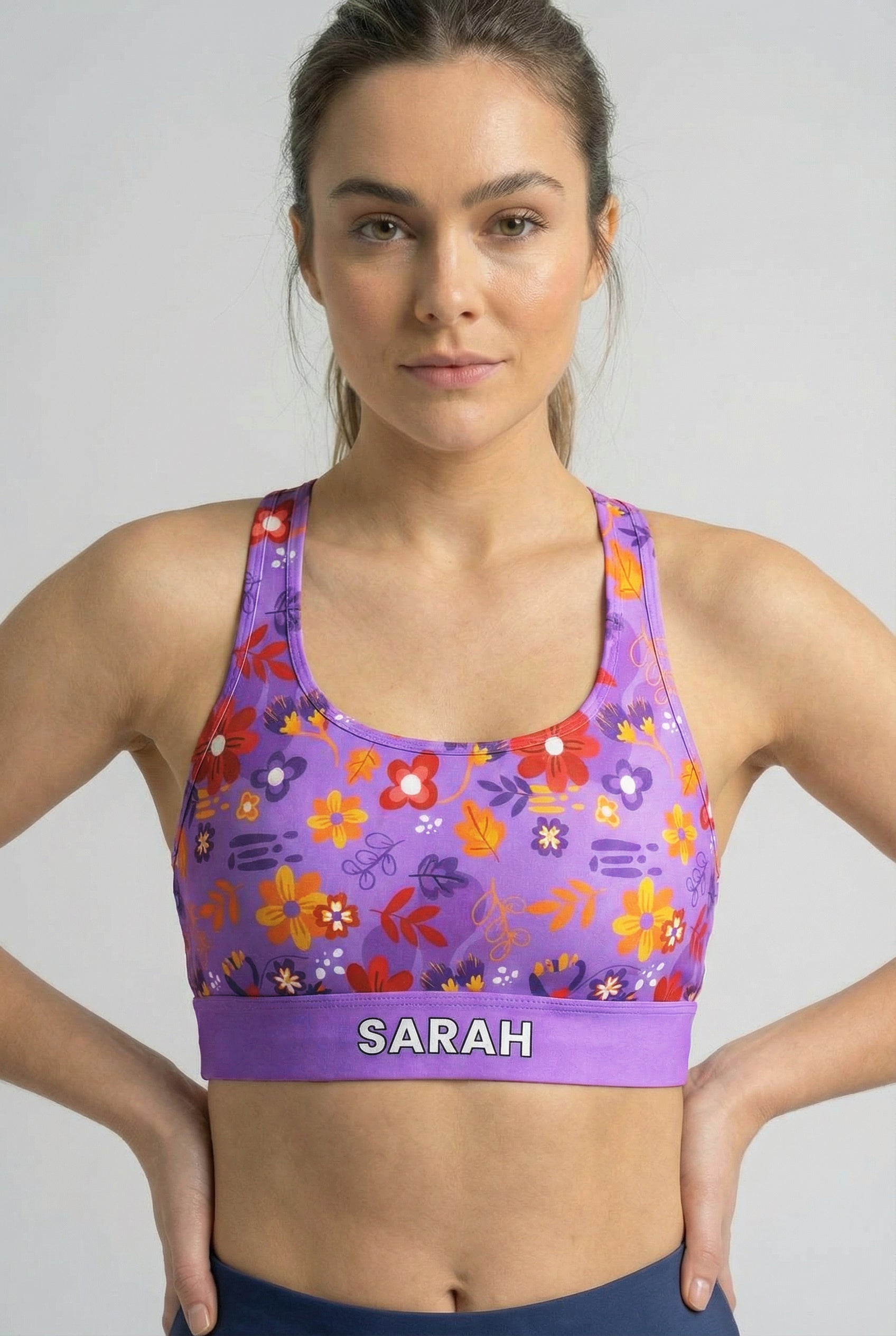 Purple sport bra with playful red and orange floral print and custom name 'SARAH' on waistband.