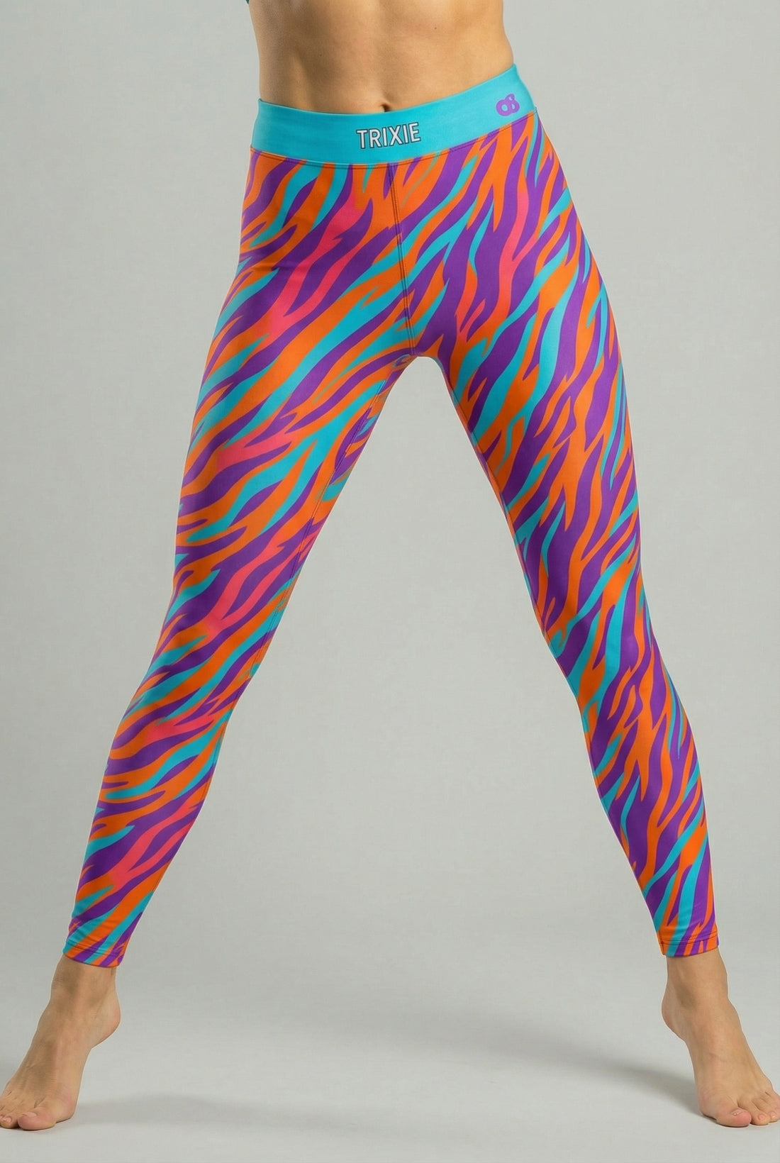 Front view of high-waisted leggings featuring orange, purple, and teal tiger stripes, with 'TRIXIE' printed on the solid teal waistband.