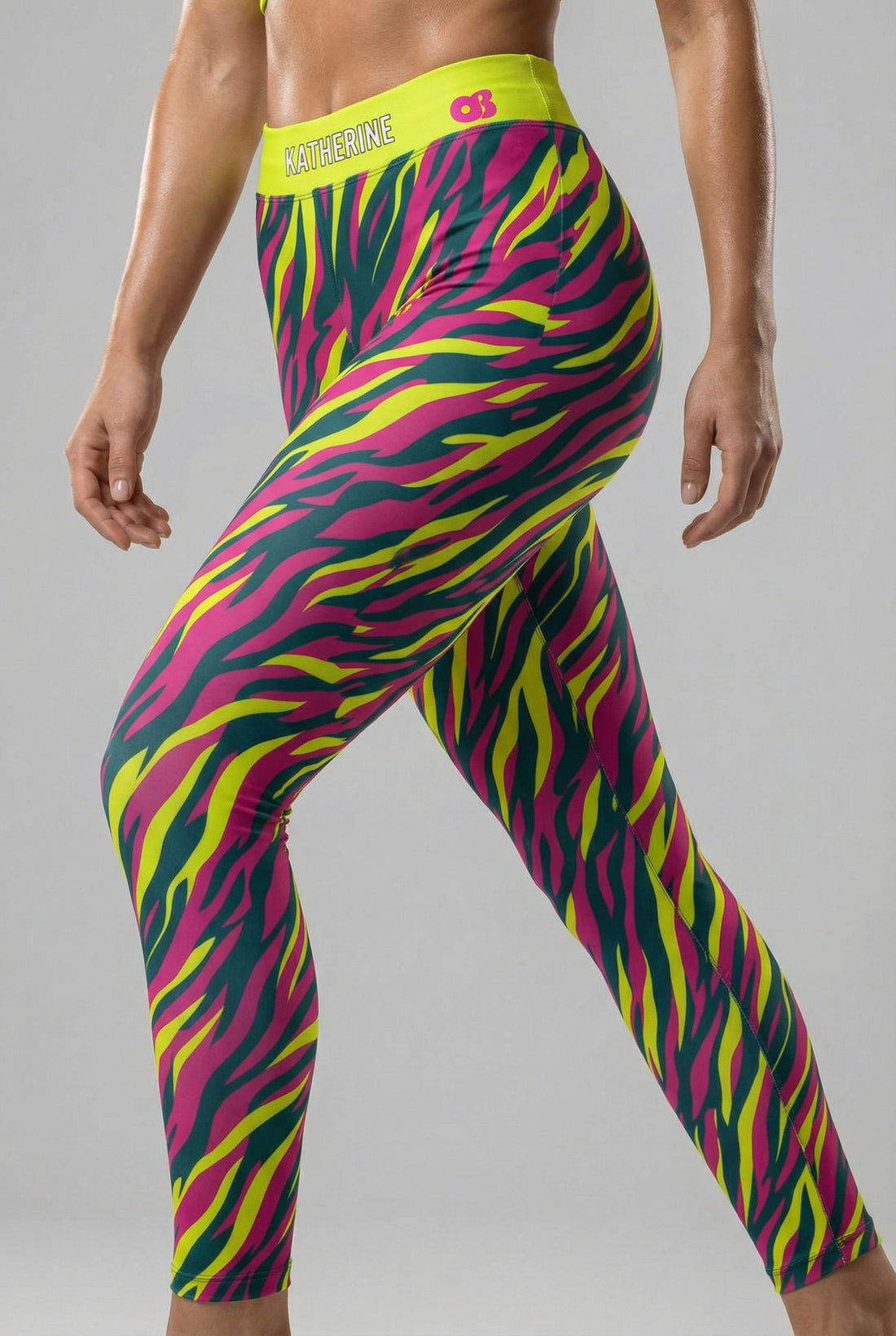 Front view of high-waisted leggings with neon magenta, yellow, and teal tiger stripes, featuring 'KATHERINE' printed on the solid neon lime waistband.