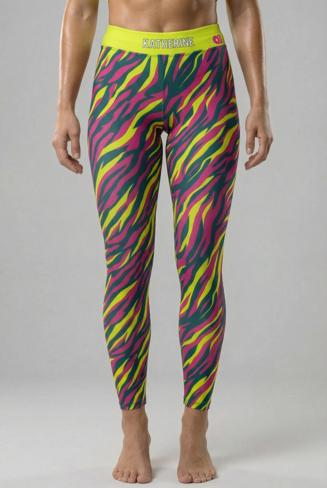 Front view of high-waisted leggings with neon magenta, yellow, and teal tiger stripes, featuring 'KATHERINE' printed on the solid neon lime waistband.