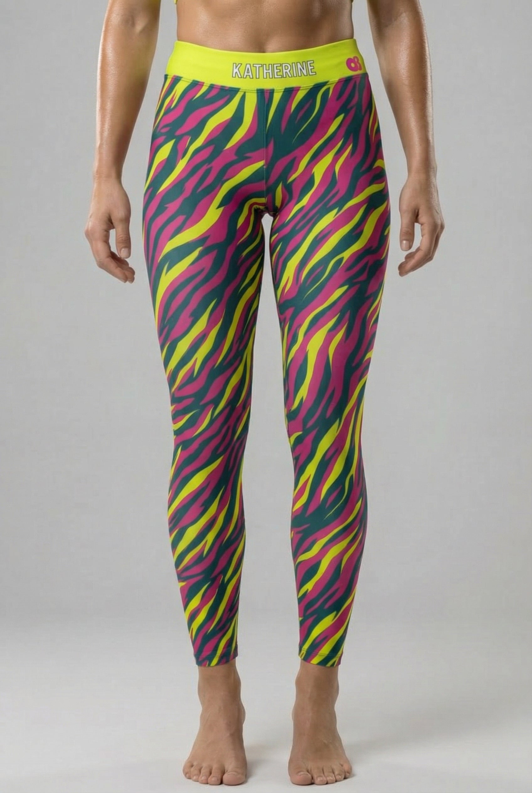 Front view of high-waisted leggings with neon magenta, yellow, and teal tiger stripes, featuring 'KATHERINE' printed on the solid neon lime waistband.