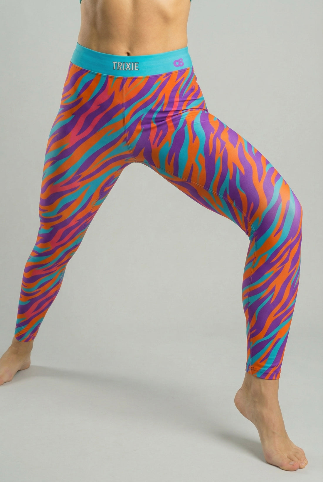 Front view of high-waisted leggings featuring orange, purple, and teal tiger stripes, with 'TRIXIE' printed on the solid teal waistband.
