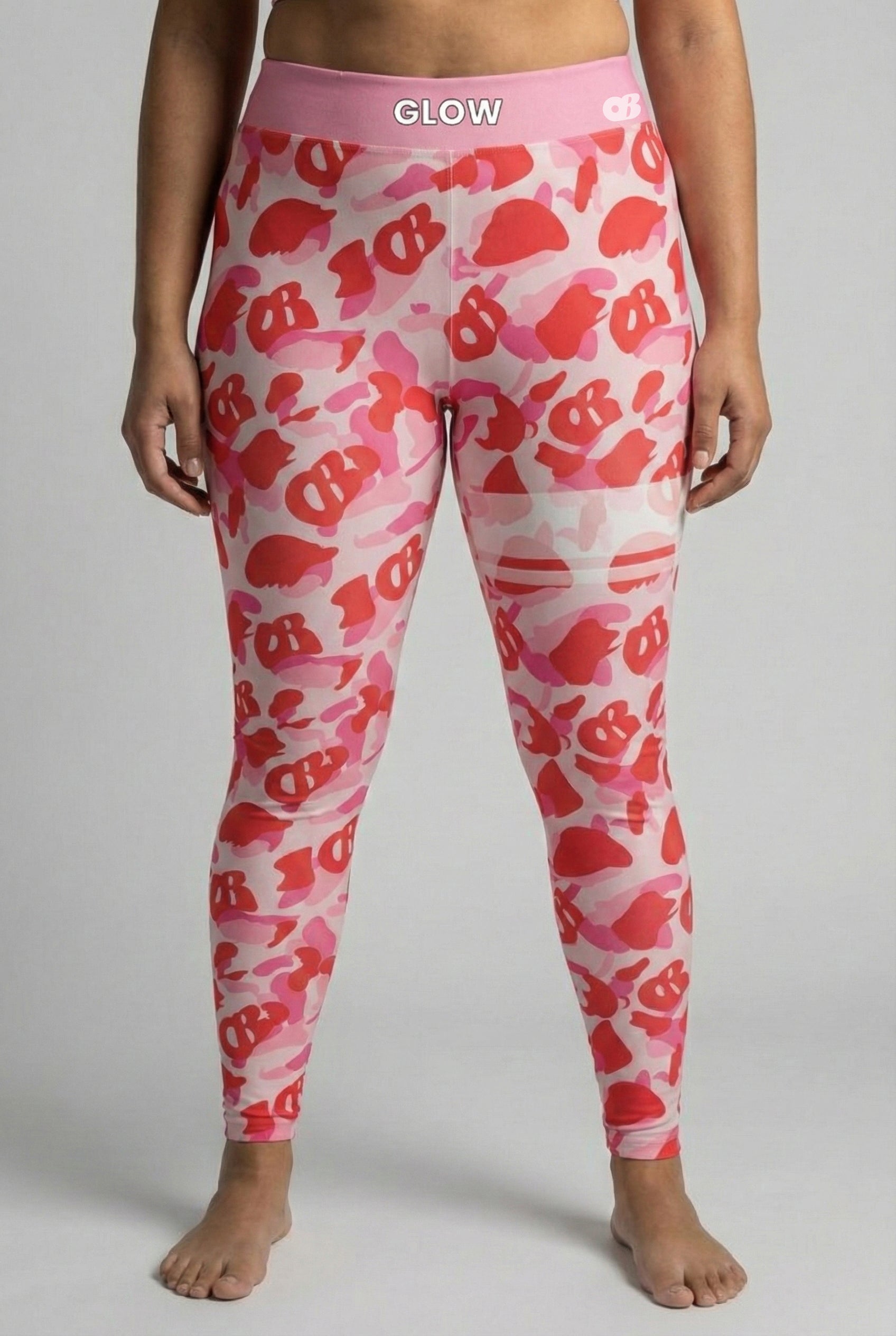 Front view of pink camouflage leggings with hidden 'OB' monogram shapes, featuring white stripes on the left thigh and 'GLOW' printed on the pastel pink waistband.