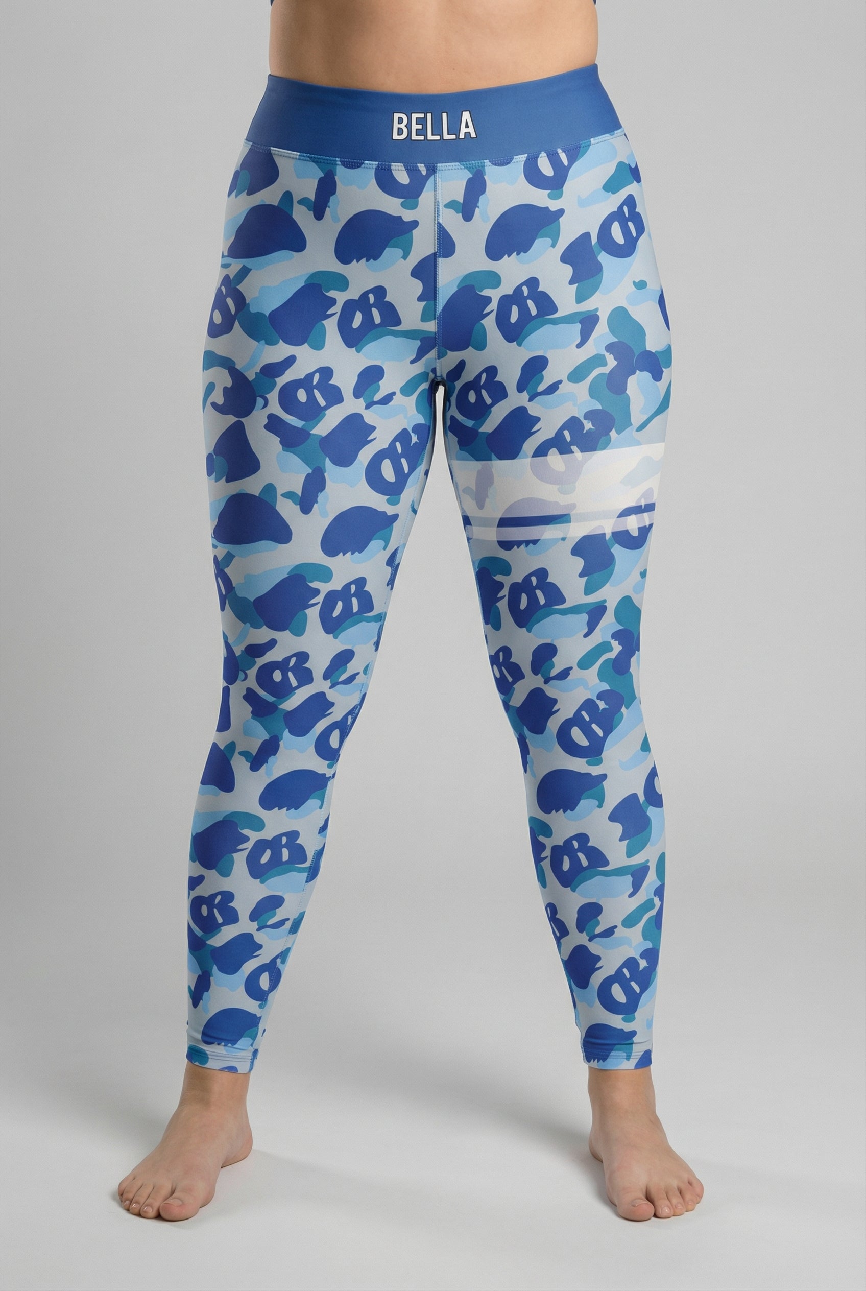 Front view of blue camouflage leggings with hidden 'OB' monogram shapes, featuring white stripes on the left thigh and 'AMA' printed on the slate blue waistband.