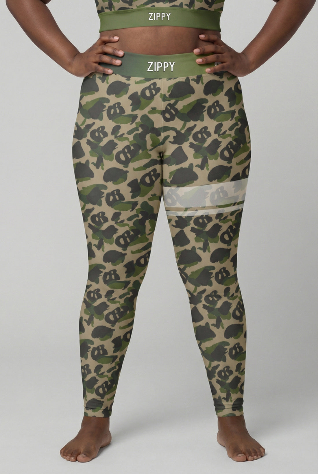 Front view of military green camouflage leggings with hidden 'OB' monogram shapes, featuring white stripes on the left thigh and 'ZIPPY' printed on the olive waistband.
