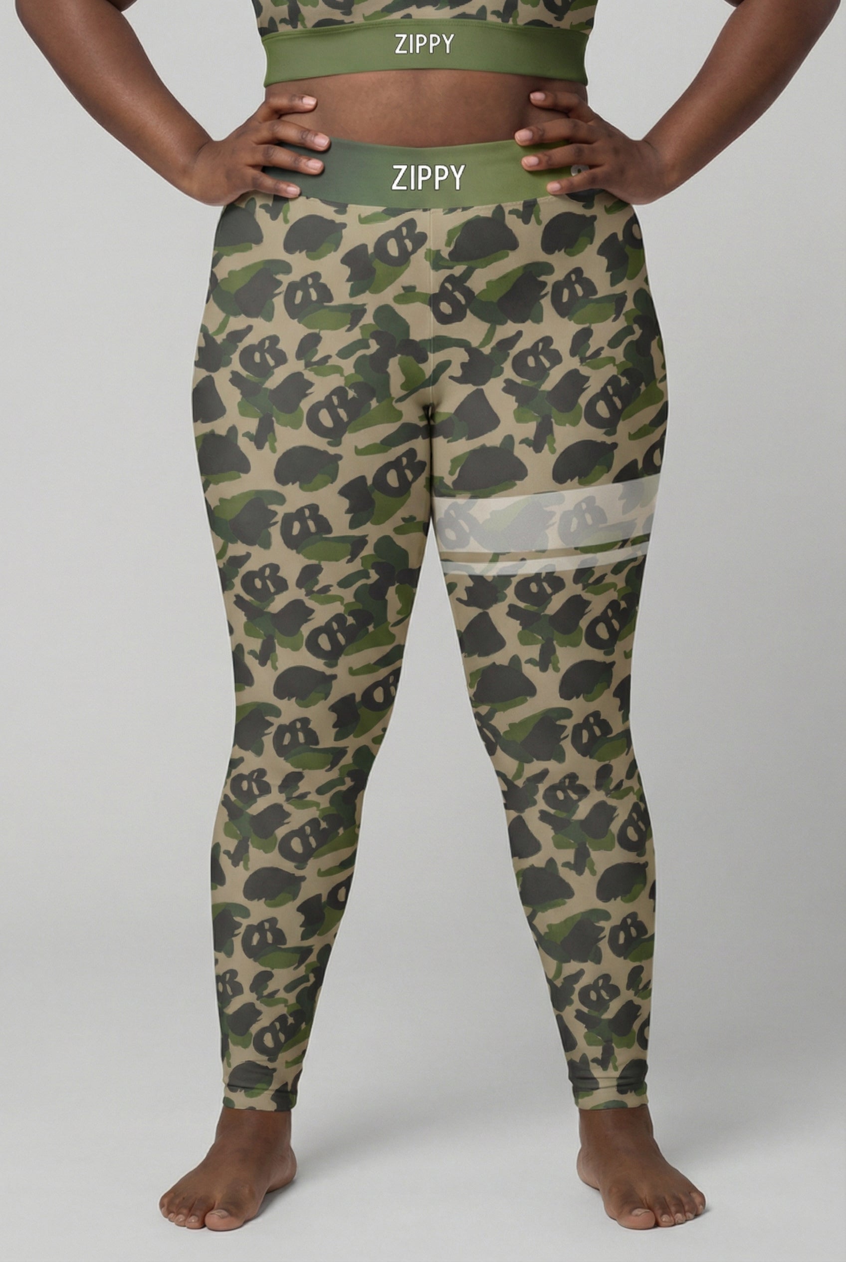 Front view of military green camouflage leggings with hidden 'OB' monogram shapes, featuring white stripes on the left thigh and 'ZIPPY' printed on the olive waistband.