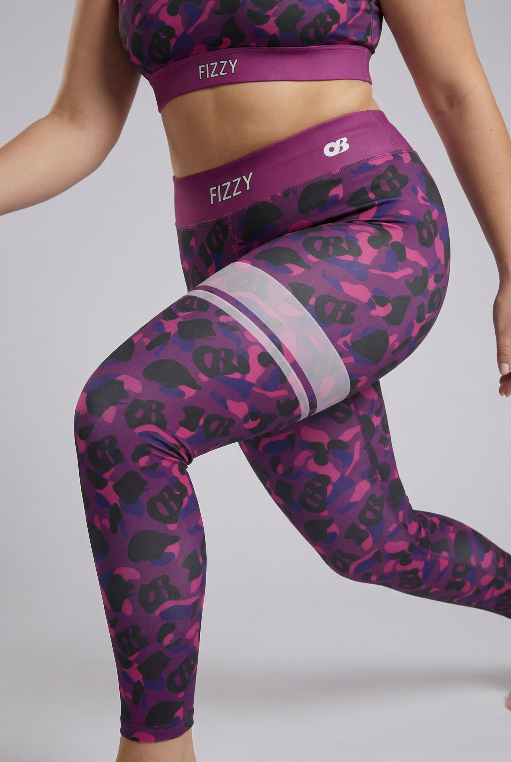 Front view of purple camouflage leggings with hidden 'OB' monogram shapes, featuring white stripes on the left thigh and 'FIZZY' printed on the plum waistband.