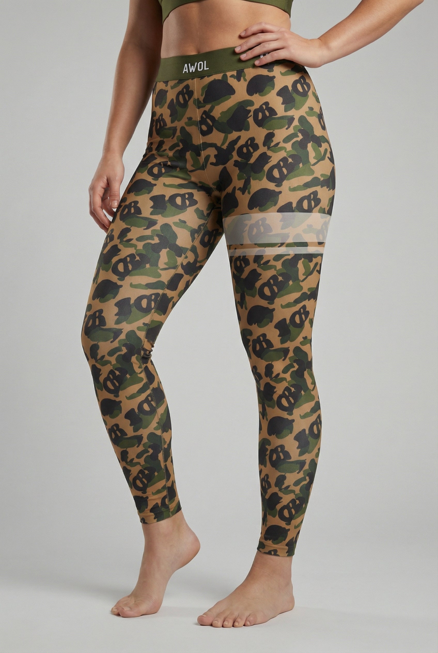 Front view of military green camouflage leggings with hidden 'OB' monogram shapes, featuring white stripes on the left thigh and 'AWOL' printed on the olive waistband.