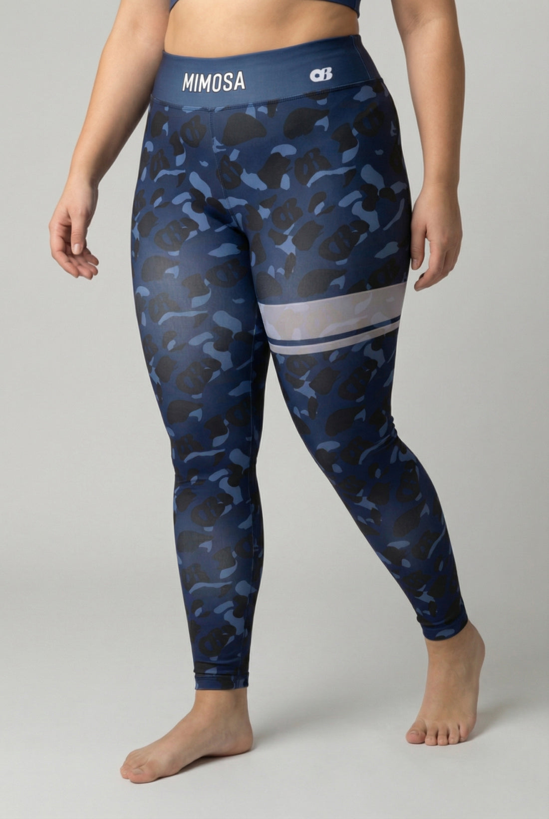 Front view of navy blue camouflage leggings with hidden 'OB' monogram shapes, featuring white stripes on the left thigh and 'MIMOSA' printed on the navy waistband.