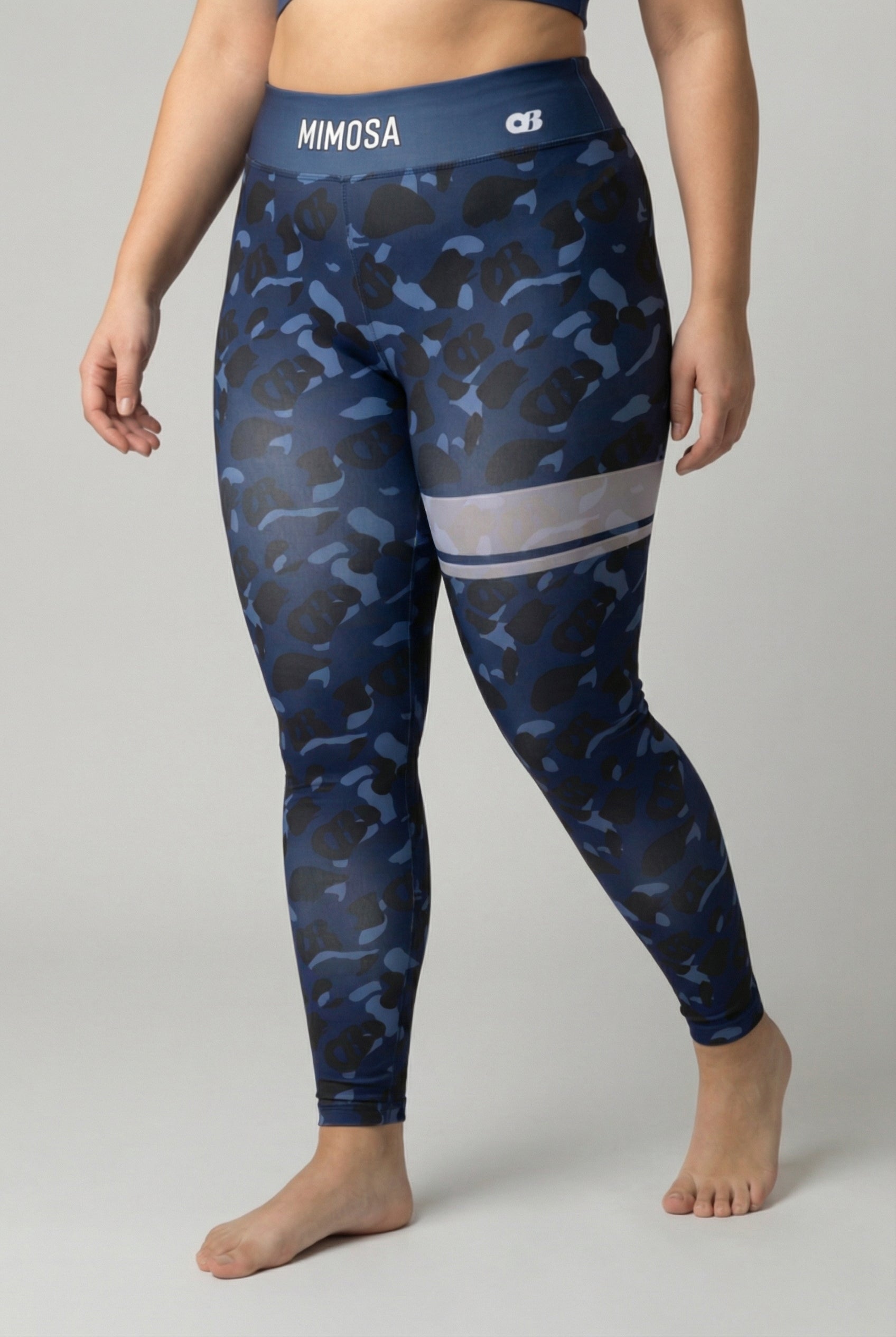 Front view of navy blue camouflage leggings with hidden 'OB' monogram shapes, featuring white stripes on the left thigh and 'MIMOSA' printed on the navy waistband.
