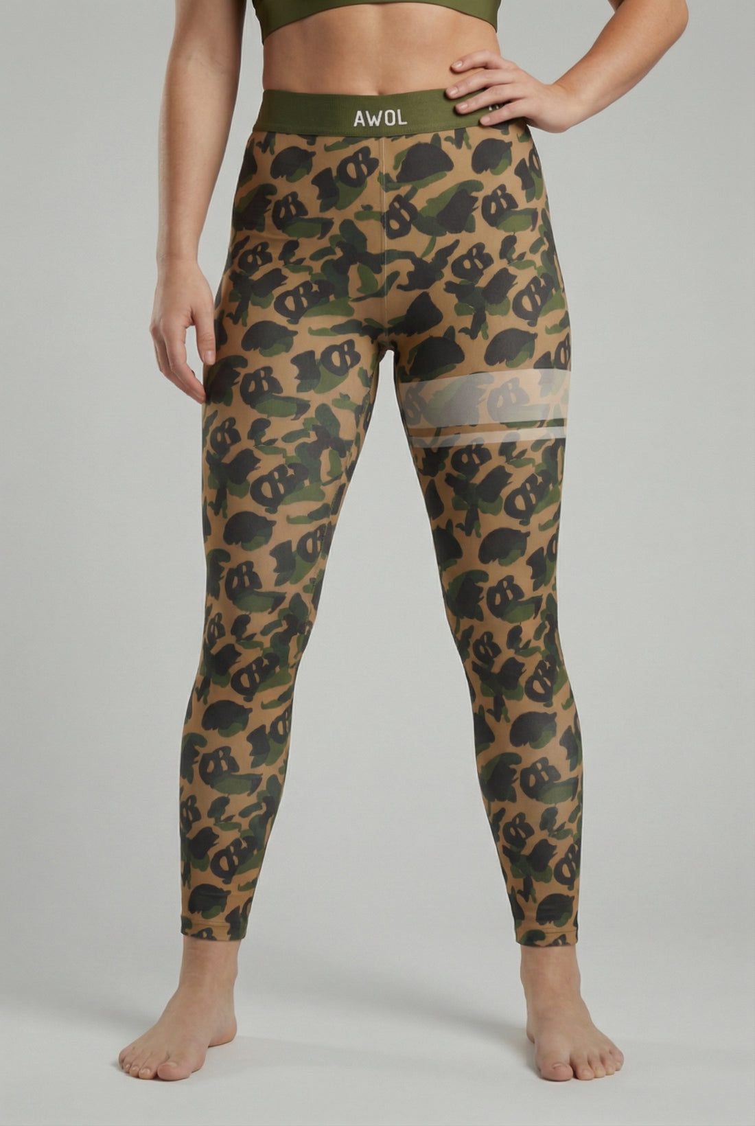 Front view of military green camouflage leggings with hidden 'OB' monogram shapes, featuring white stripes on the left thigh and 'AWOL' printed on the olive waistband.