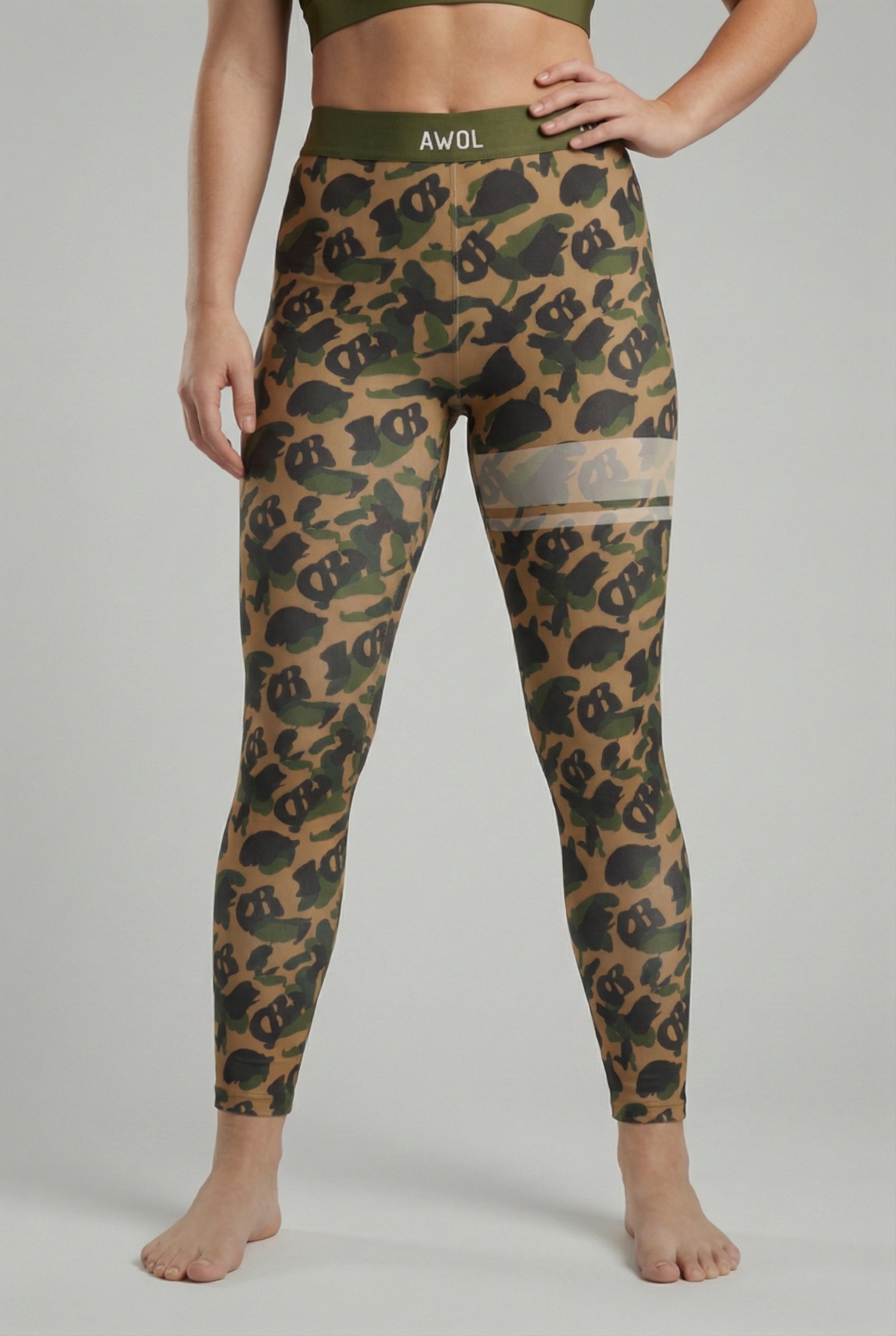 Front view of military green camouflage leggings with hidden 'OB' monogram shapes, featuring white stripes on the left thigh and 'AWOL' printed on the olive waistband.