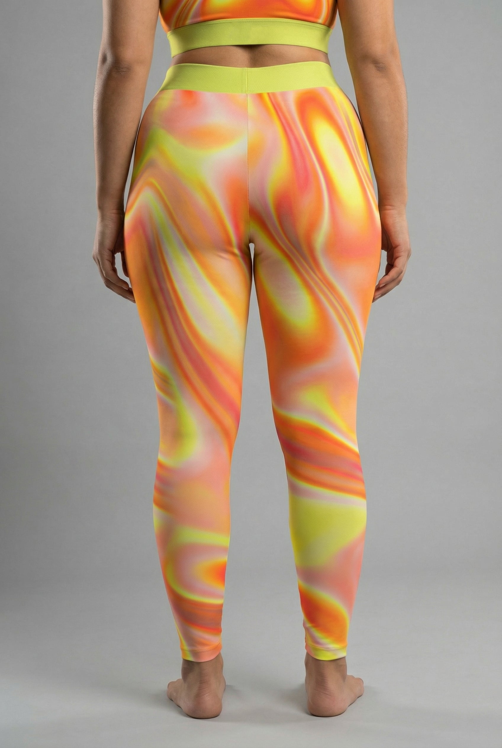 Front view of high-waisted tie-dye leggings in orange, yellow, and red swirls, featuring 'AIRY' printed on the neon lime green waistband.