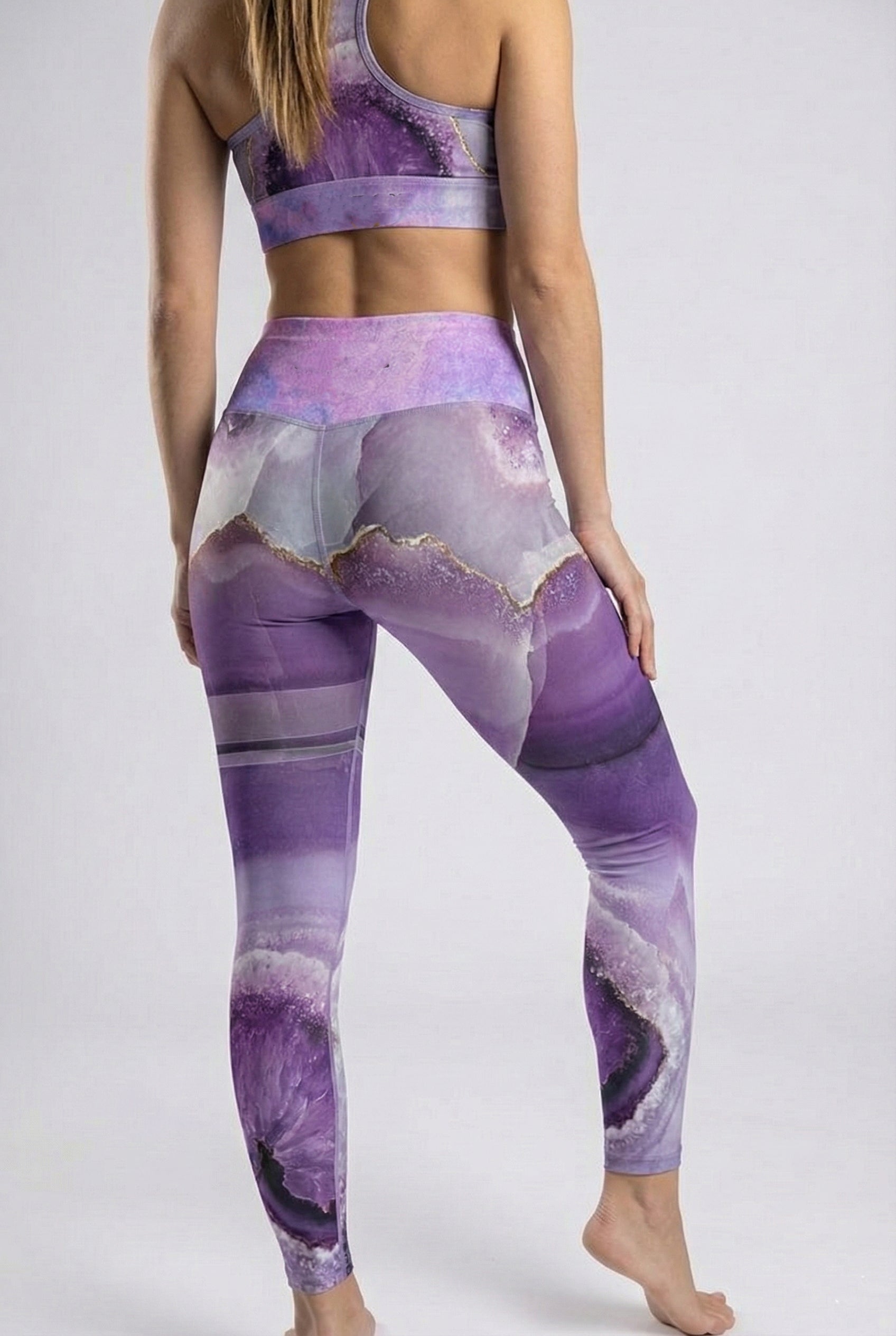 Person wearing a purple and gray patterned sports bra and leggings on a white background